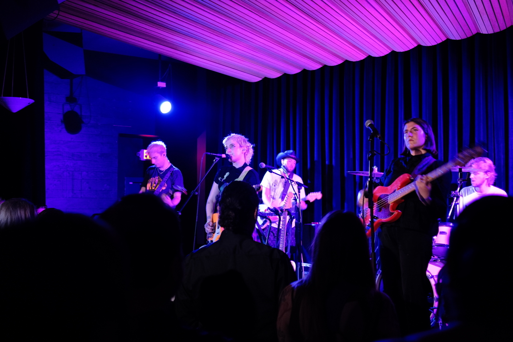 A band is performing on stage under colorful lights in front of an audience.