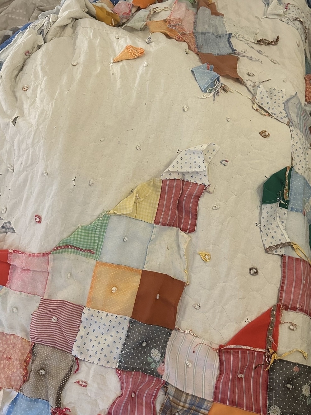 A colorful, patchwork quilt with various patterned and solid fabric squares displays some wear and tear.