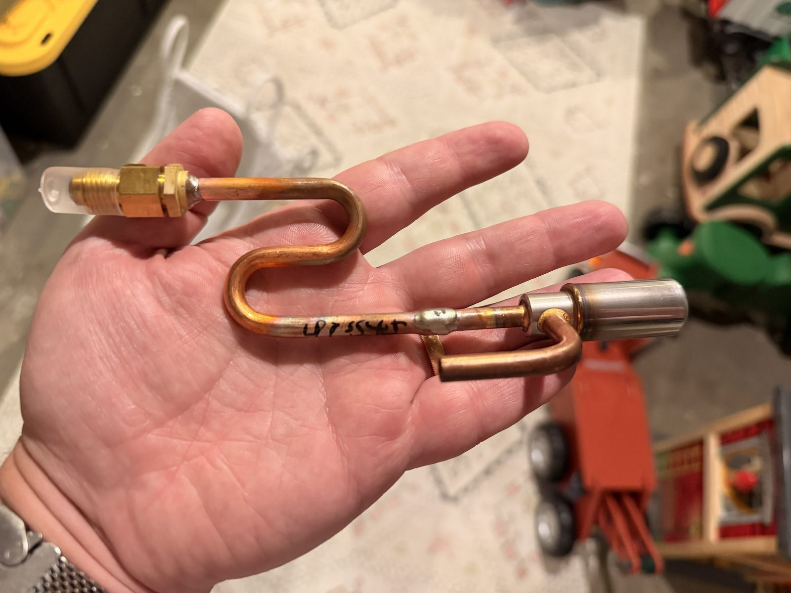 A small copper and brass expansion valve assembly held in a hand, hand-marked UPSTAIRS in black marker