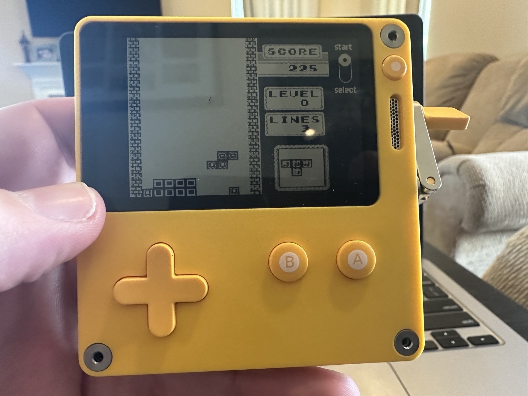 A yellow handheld gaming system with a grayscale screen running the original Nintendo Gameboy version of Tetris