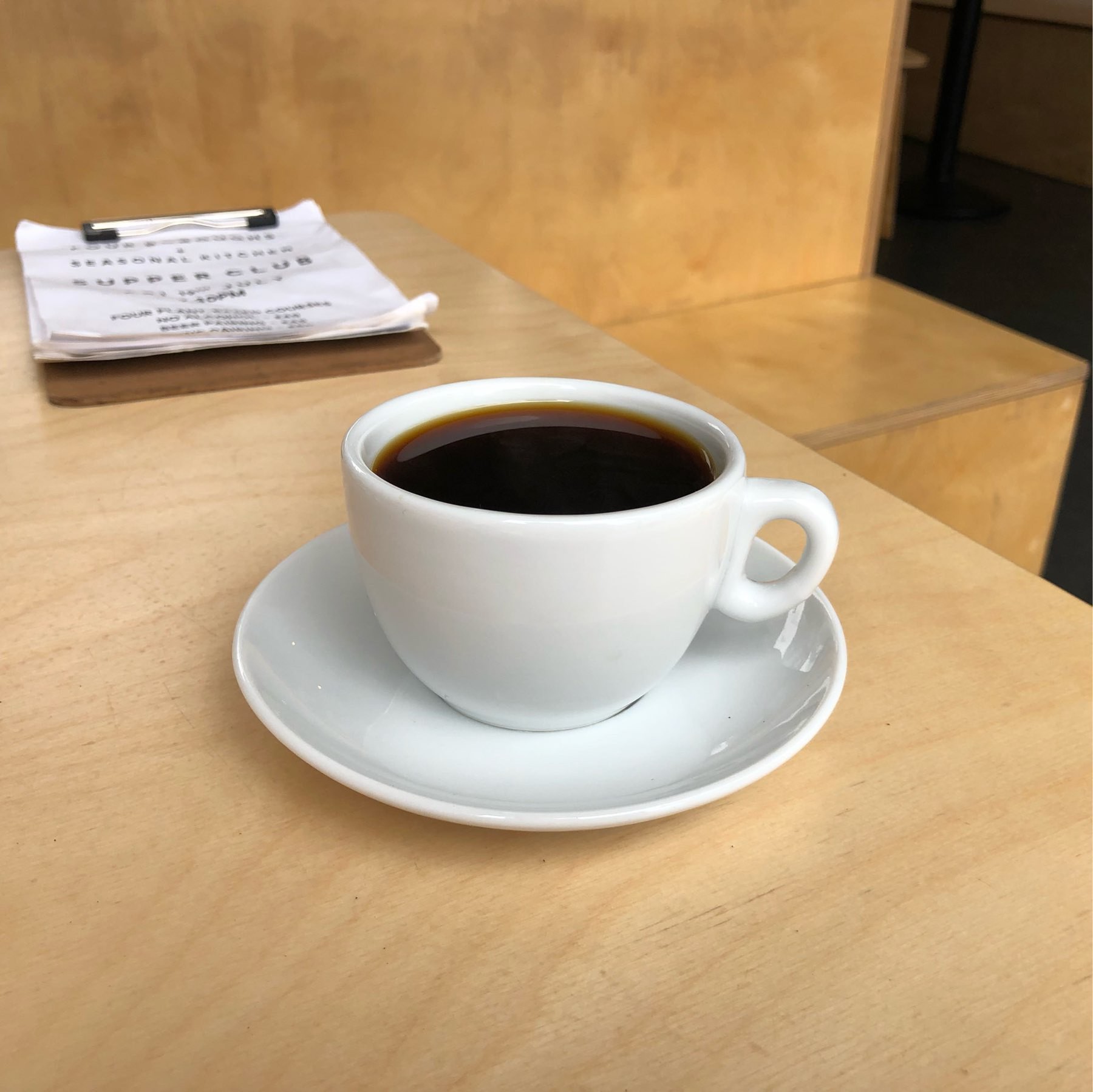 Black coffee in a white cup with a white saucer on a wood table