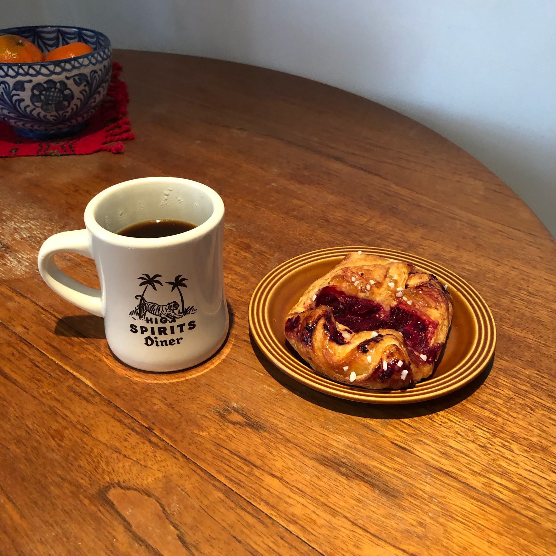 Black coffee on a dinner mug with cherry danish pastry on a warm brown plate and teak table.