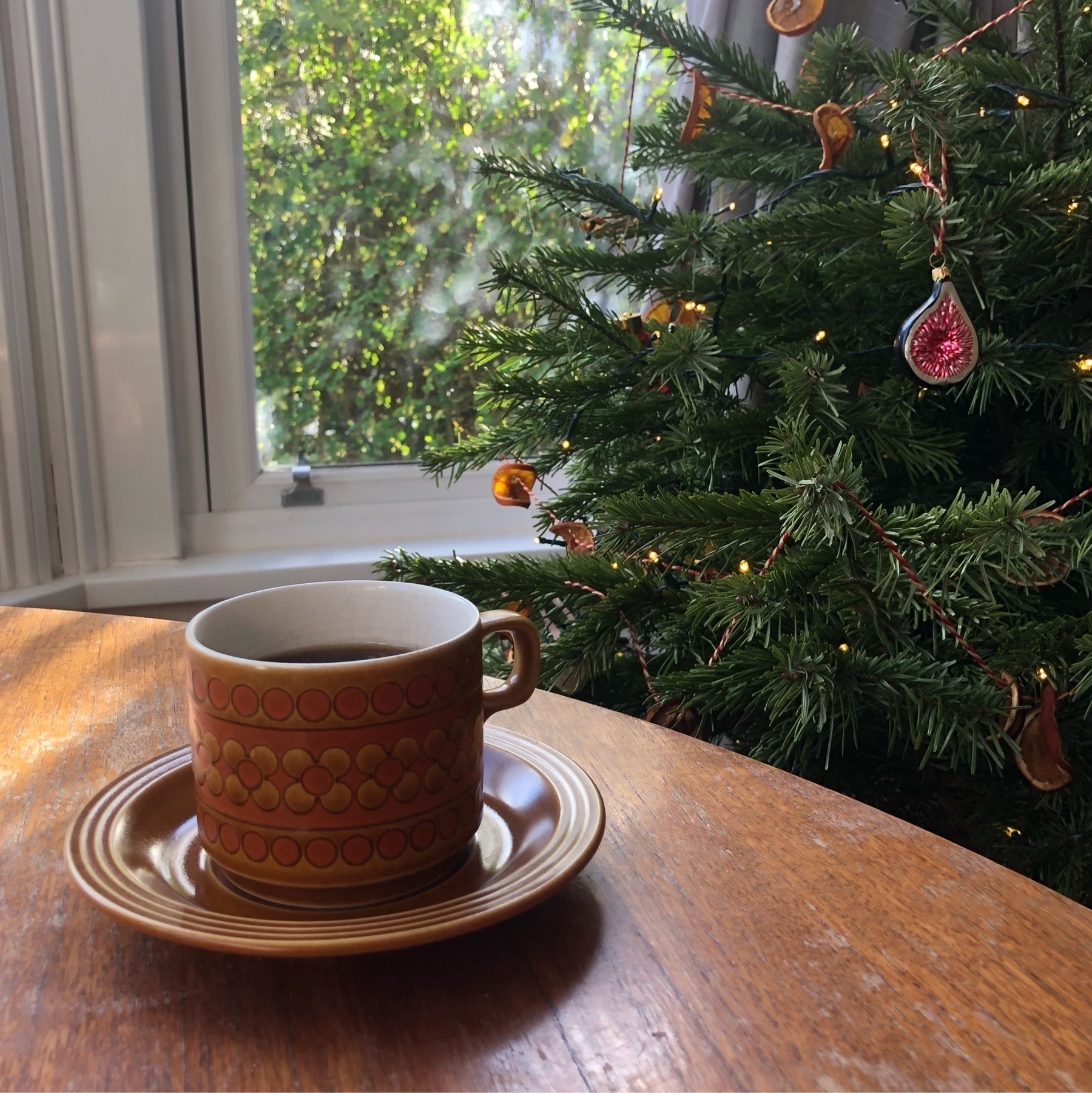 brown coffee cup and saucer next to the christmas tree