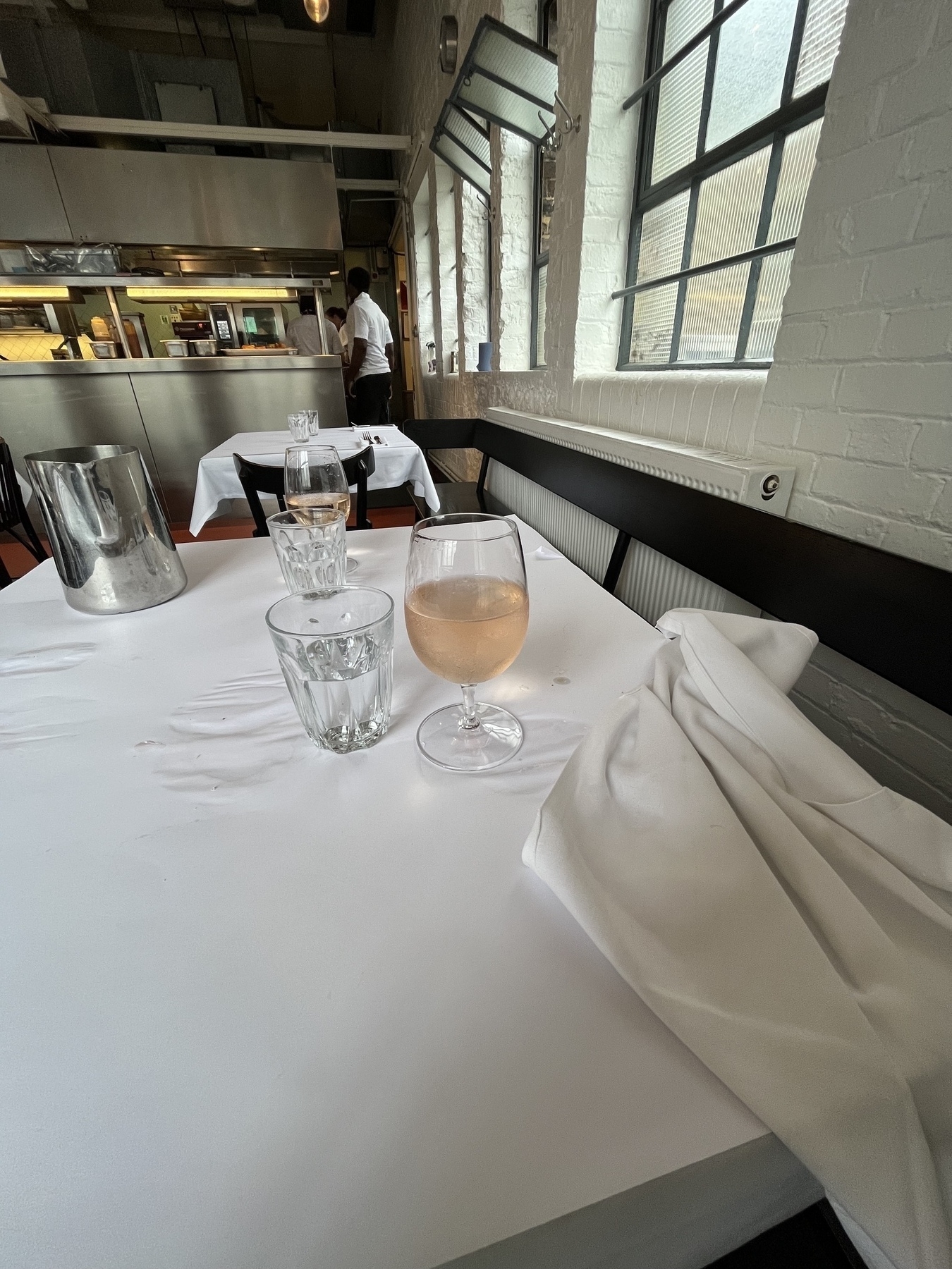 Pink wine on top of a table with a white cloth, water glass, background of a restaurant, metal jug