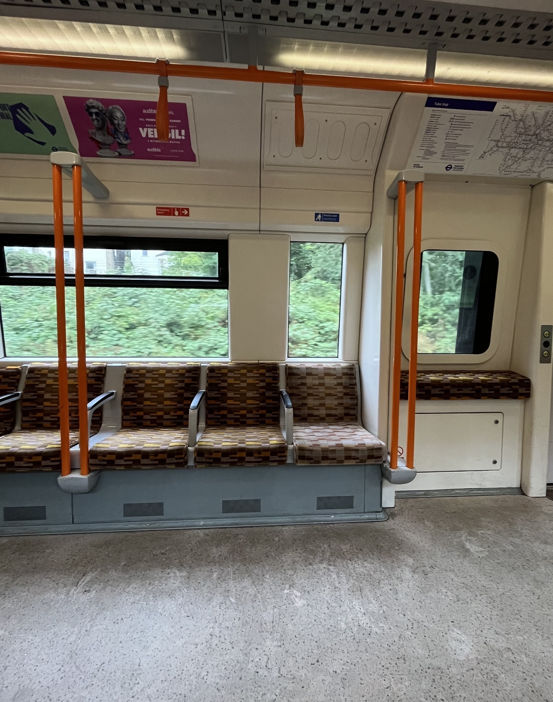 Row of empty seats in a overground train carriage, orange and brown seats, greenery out of the window 