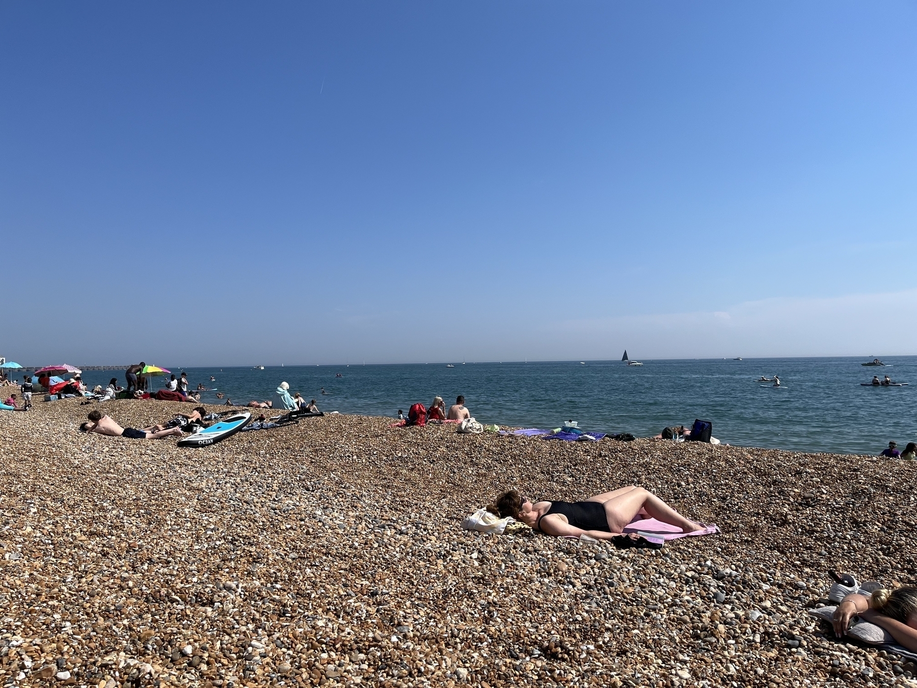 People laying in a pebble beach, clear skies, people are swimming