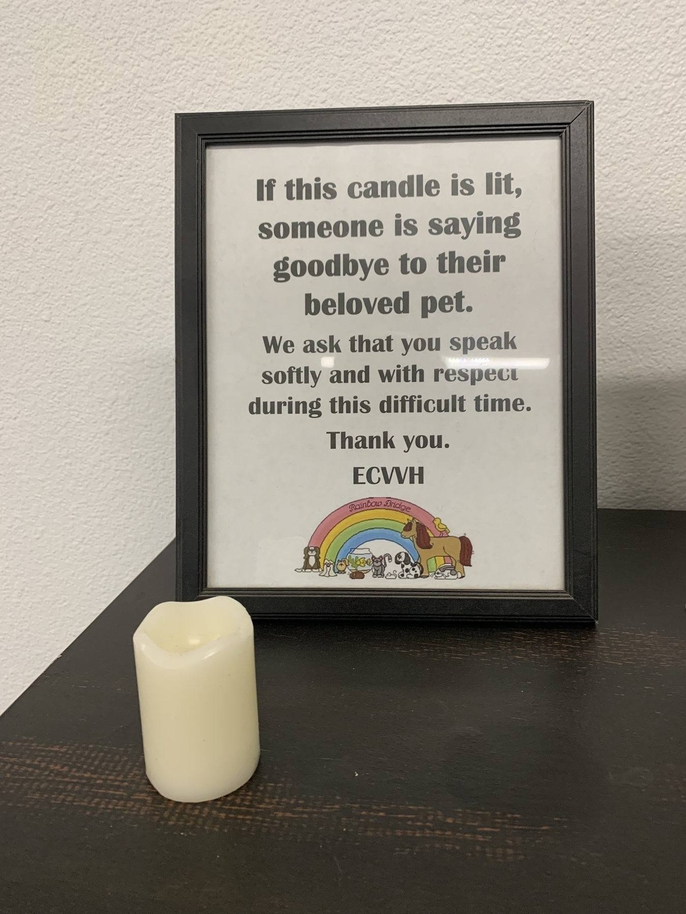 The simple sign, with a rainbow symbol, is next to a candle. The sign reads, “If this candle is lit, someone is saying goodbye to their beloved pet. We ask that you speak softly and with respect during this difficult time. Thank you.”