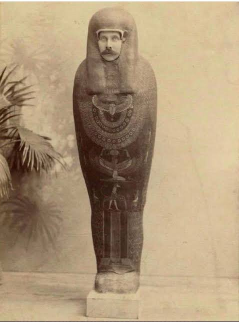 An old photograph featuring a person with a mustache posing inside an Egyptian sarcophagus, giving the illusion that the sarcophagus has a human face.
