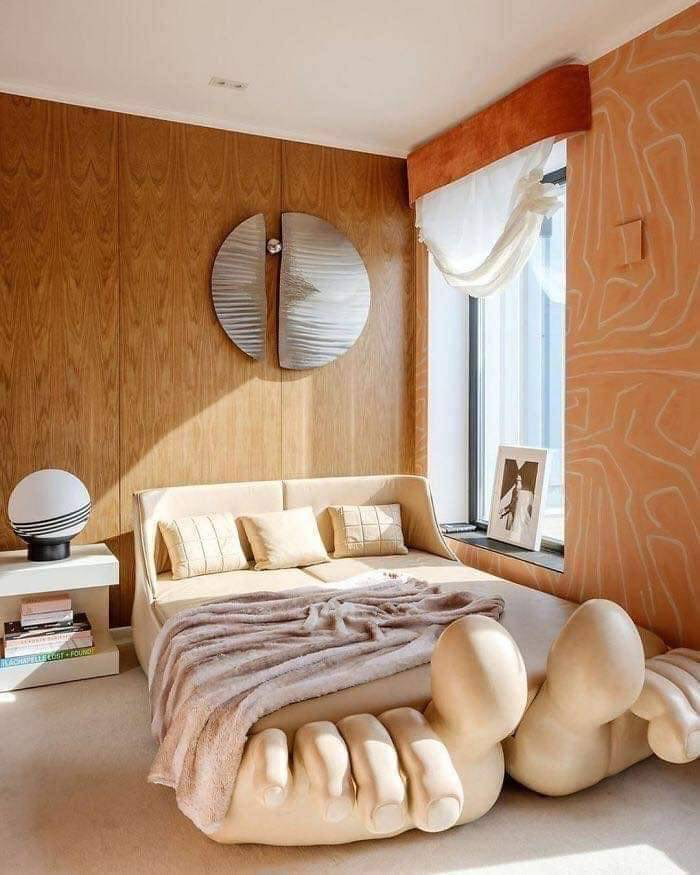 A unique bedroom with wood-paneled walls, a bed designed to look as if it’s resting on a giant hand, and a foot-shaped base at the foot of the bed. 