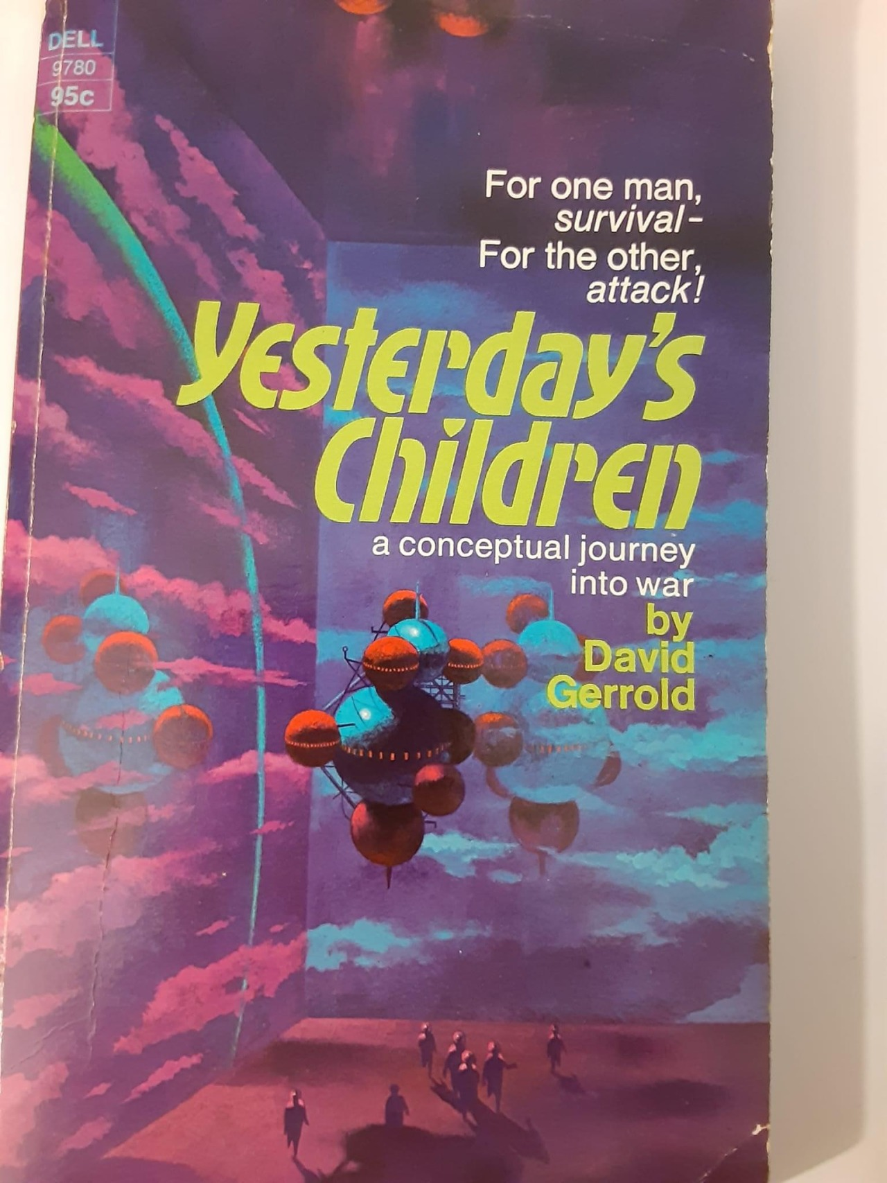 Close-up photo of a thin paperback book with an abstract cover illustration of a starship comprising about a dozen attached spheres of various sizes stuck together like Tinkertoys, hanging inside what looks like a bare cubical room with purple and blue walls covered in clouds. On the floor of the room are about a dozen stylized human figures. The lettering on the cover reads, 'For one man _survival_ — for the other, _attack!_ Yesterday's Children a conceptual journey into war by David Gerrold.'