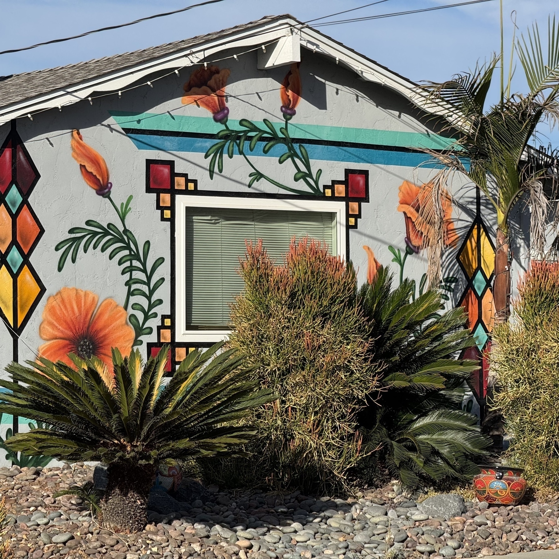 A house decorated with colorful floral murals and surrounded by plants and shrubs.