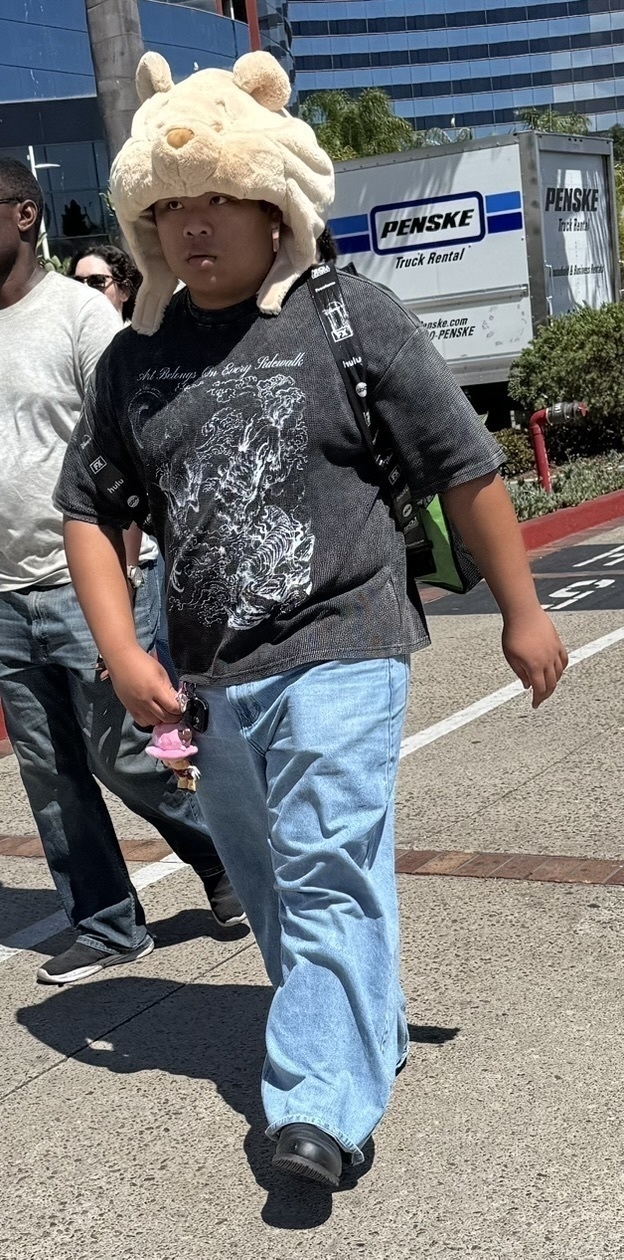 Auto-generated description: A person wearing a bear hat and casual clothing is walking outdoors near a Penske truck.