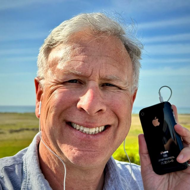 Phil Schiller wearing headphones plugged into an iPhone 3GS.