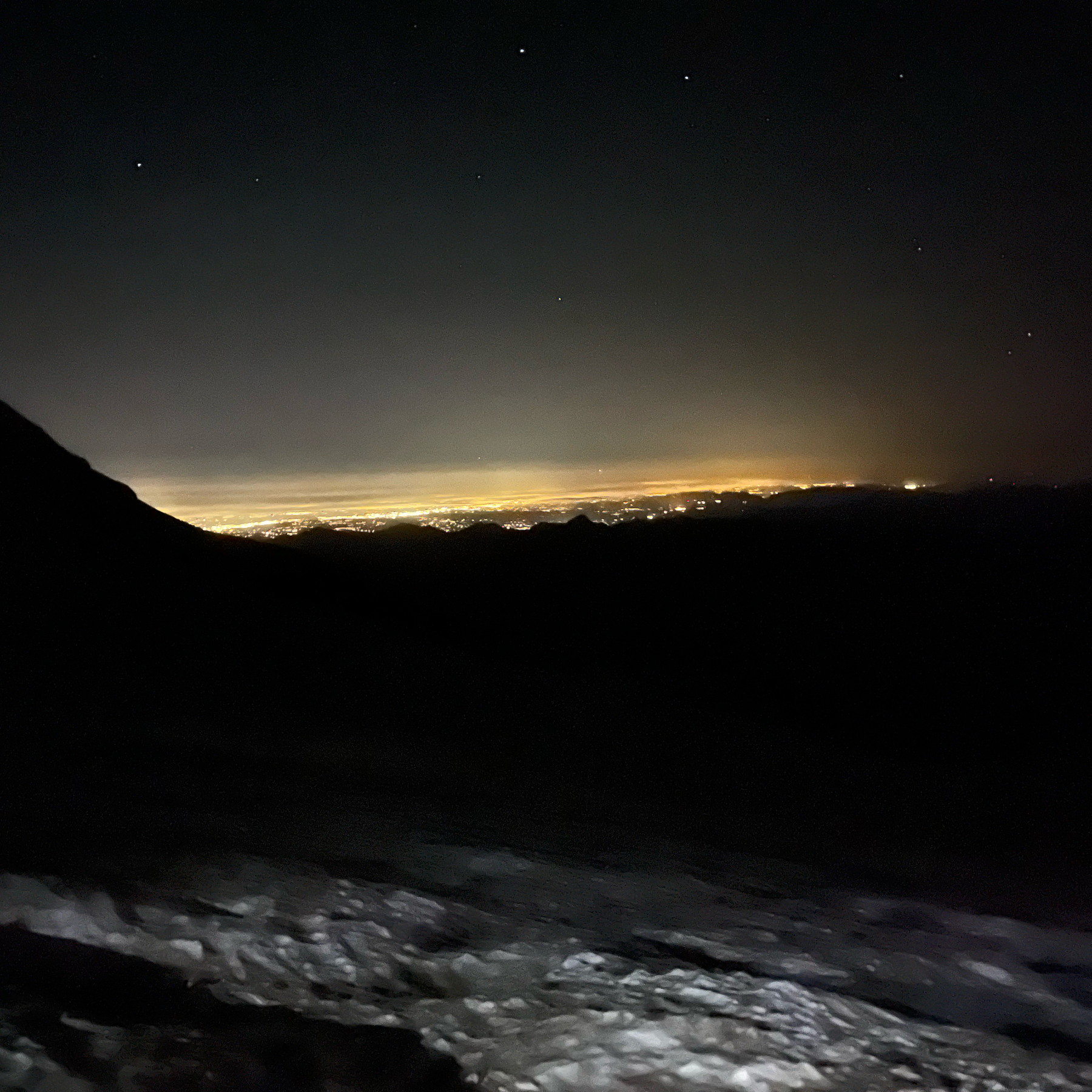 A lightened city as seen in the distance from a mountainside in pitch dark.
