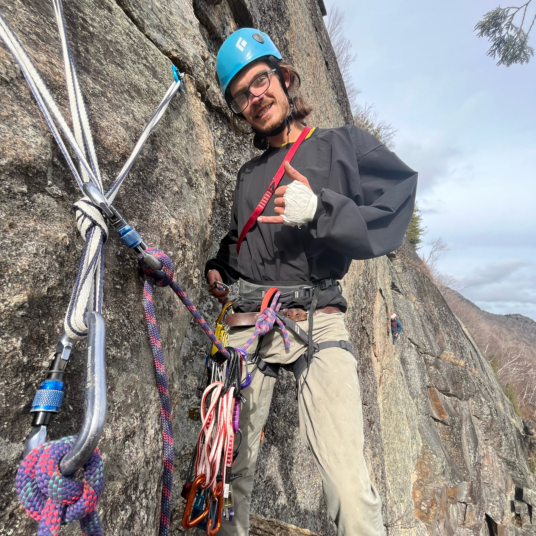 A climber attached to the rock wall with a sling and purple rope.