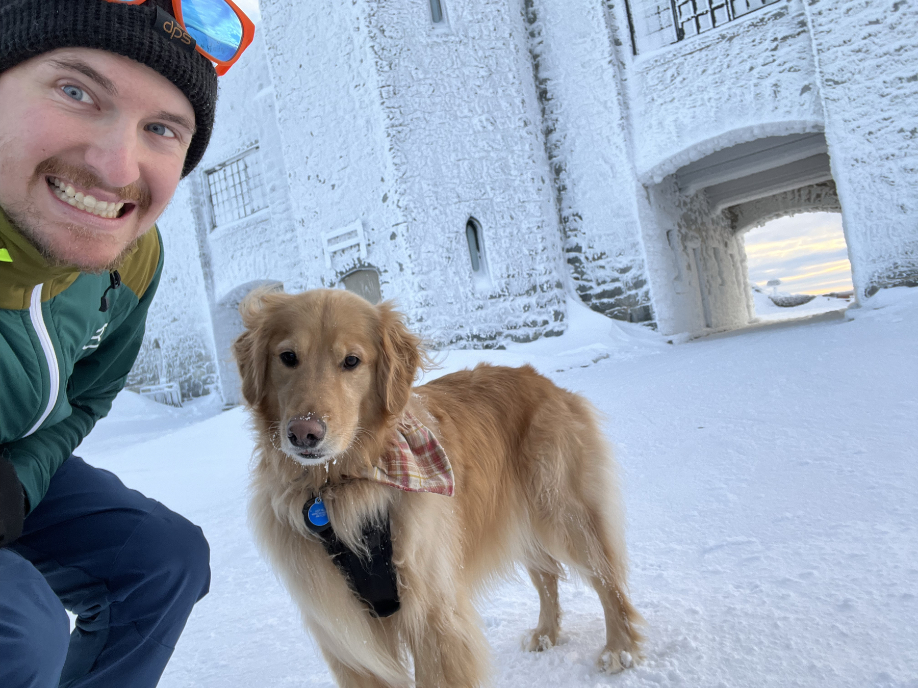Man with golden retriever dog behind him in front of a ice covered castle.