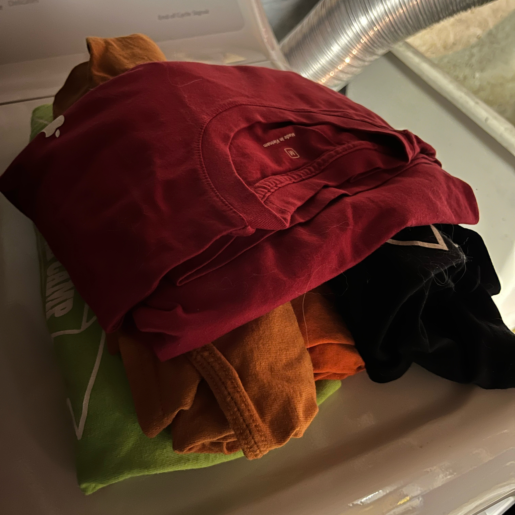 Various colored t-shirts in a pile on the dryer.