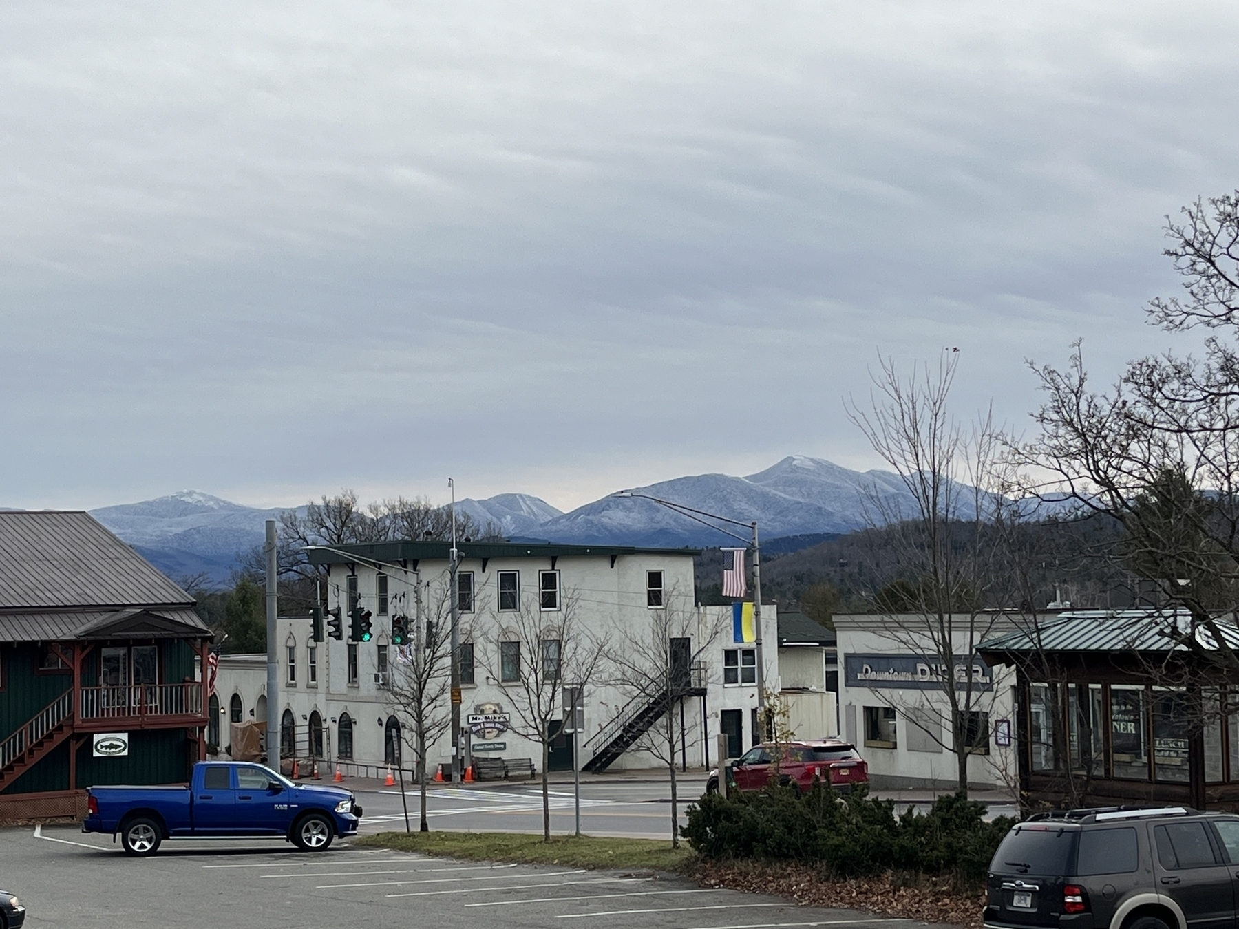 A mountain topped with a layer of snow in the background behind a local main street.