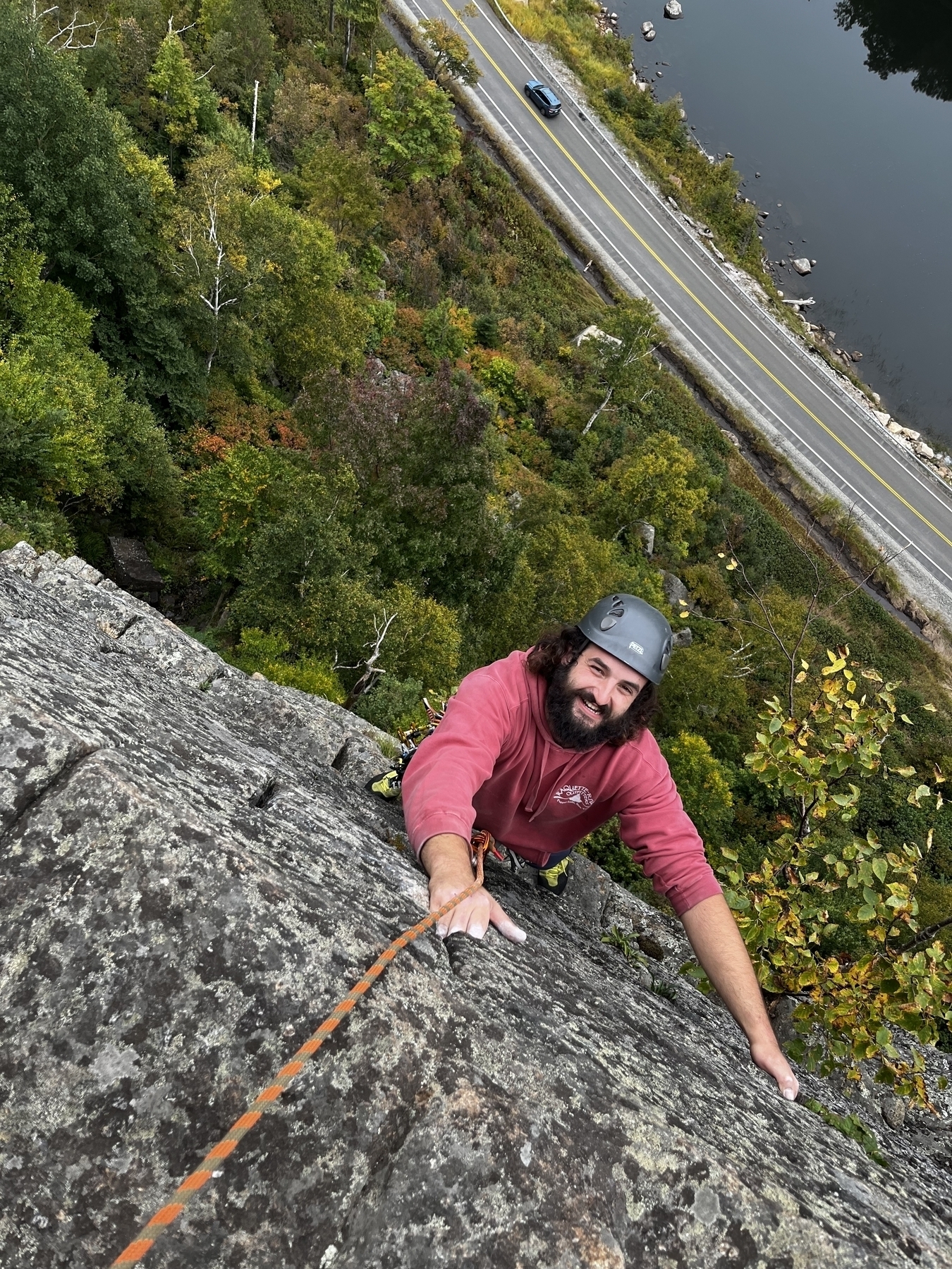 Looking down a steep mountain cliff with a bearded man climbing up it looking at the camera.