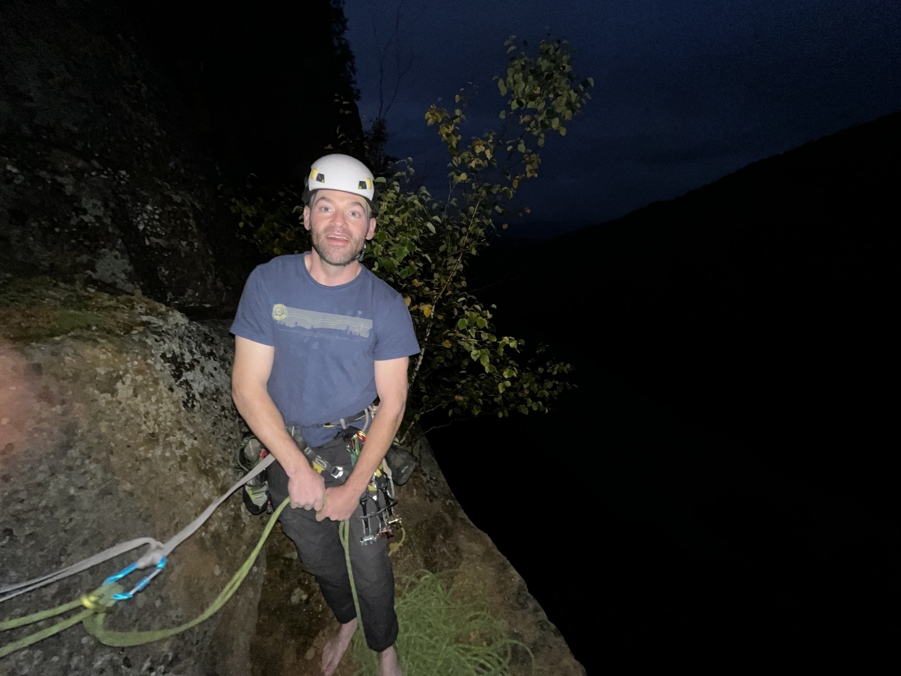 Flash photo of climber at the top of a cliff at night.