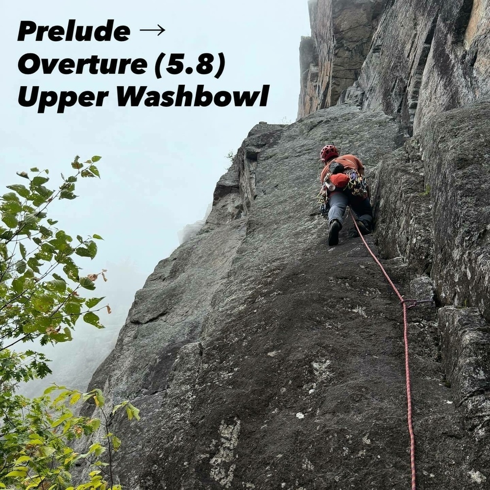 A climber ascends a steep rock face using a rope and gear, surrounded by a misty environment with some greenery. Text reads Prelude Overture (5.8) Upper Washbowl.