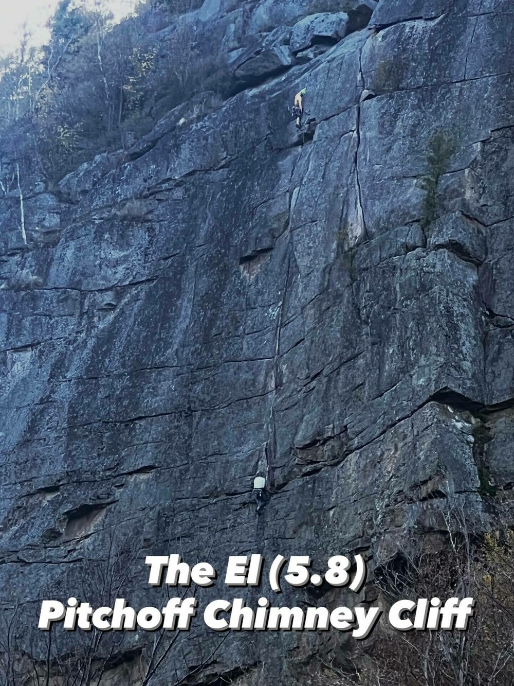 Two climbers scaling a large rock face with visible cracks at Pitchoff Chimney Cliff surrounded by trees. Text reads The El 5.8 Pitchoff Chimney Cliff.