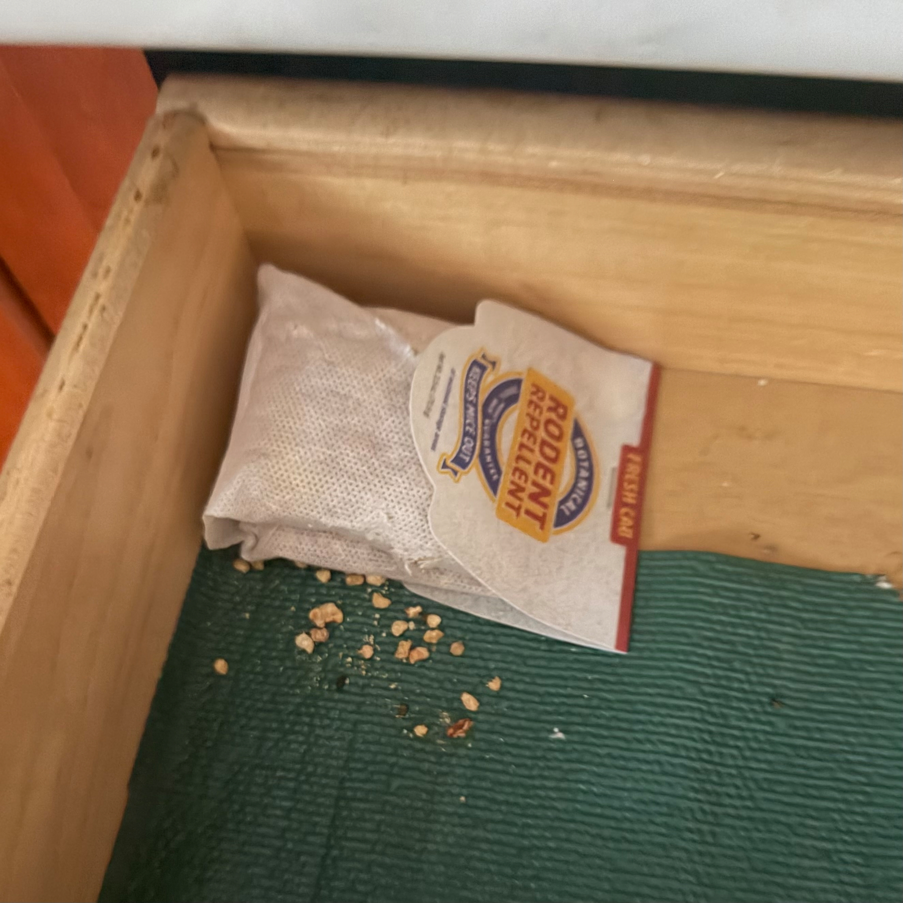 A packet of rodent repellent and some scattered granules nibbled from it are seen inside an open drawer.