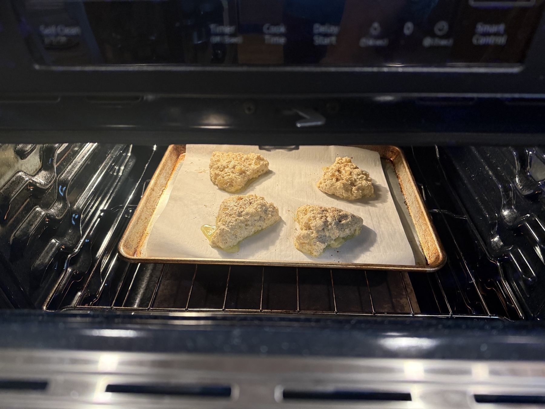 Scones are baking on a parchment-lined baking sheet inside an oven.