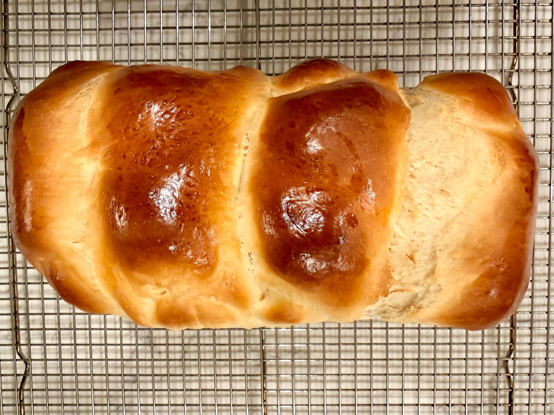A freshly baked, golden-brown loaf of bread is resting on a cooling rack.