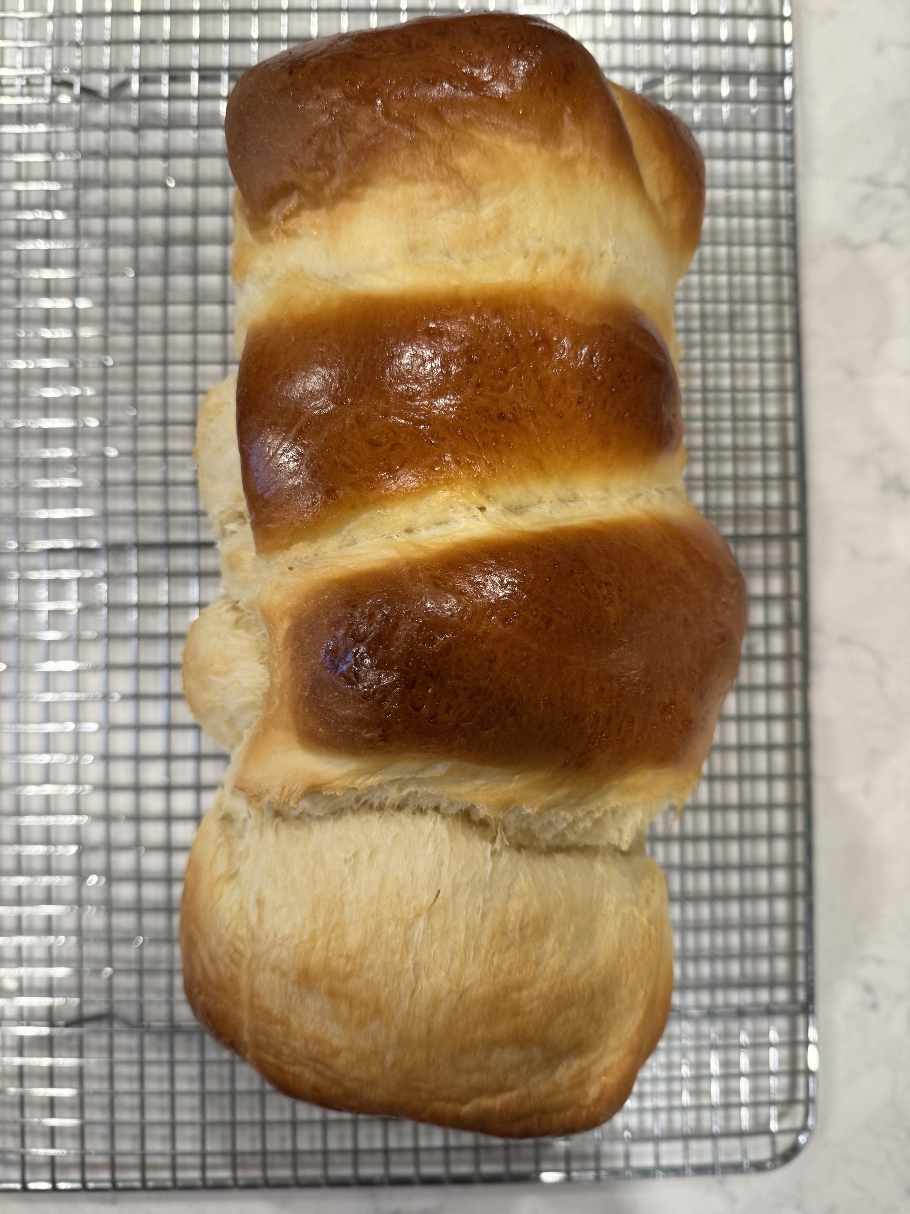 A loaf of golden-brown bread is cooling on a wire rack.