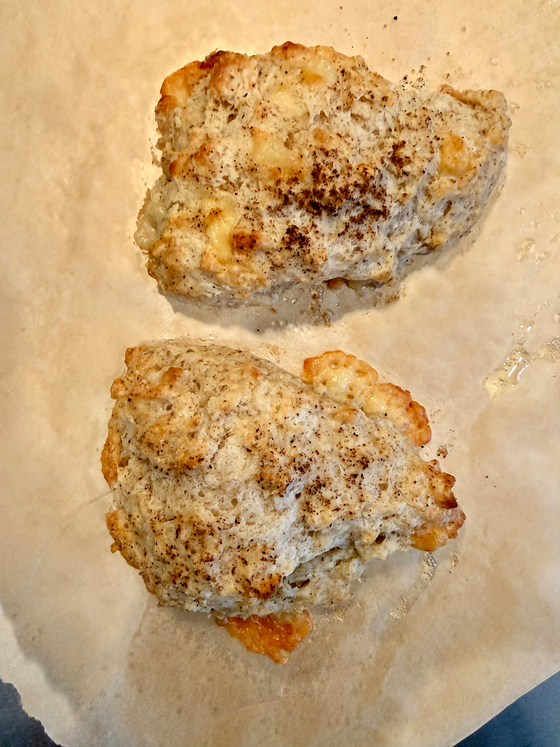 Two freshly baked, golden-brown scones with visible cheese bits on parchment paper.