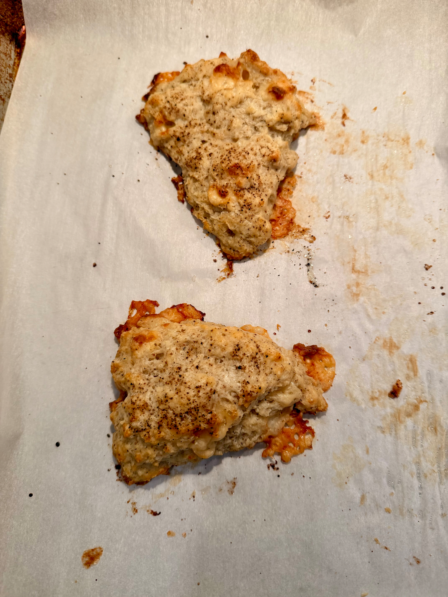 Two baked scones sit on a parchment-lined baking sheet.