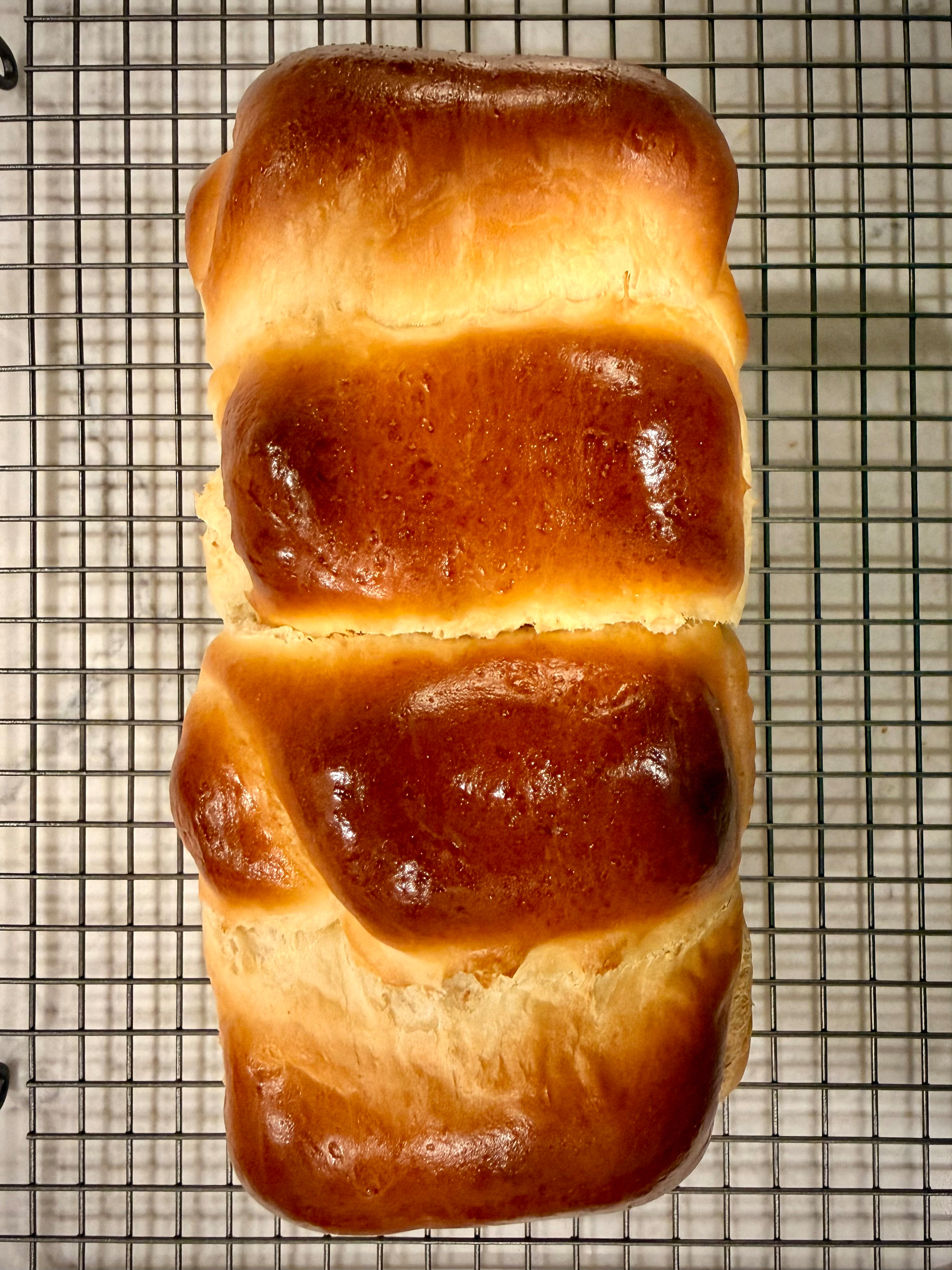A freshly baked loaf of brioche bread is resting on a cooling rack.