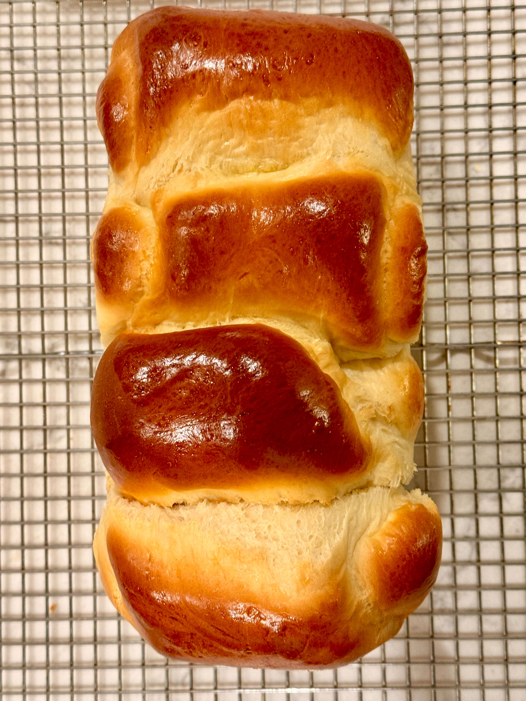A loaf of shiny, golden-brown bread is cooling on a metal wire rack.
