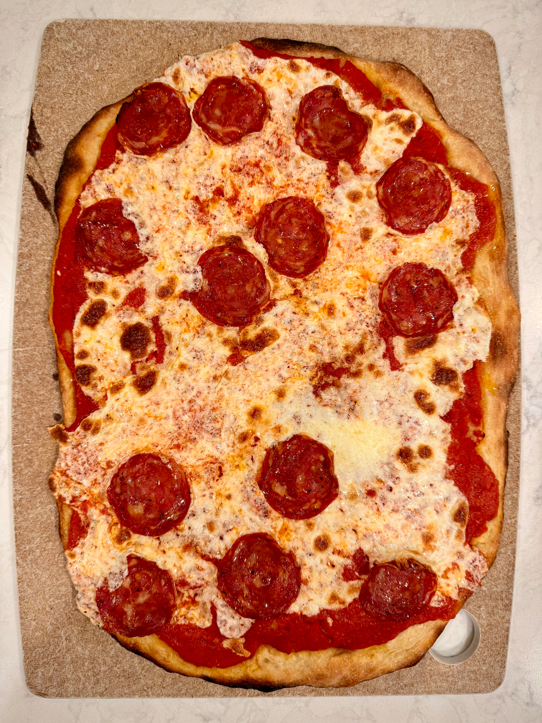 A rectangular pepperoni pizza with a thin crust is topped with melted cheese and slices of pepperoni.