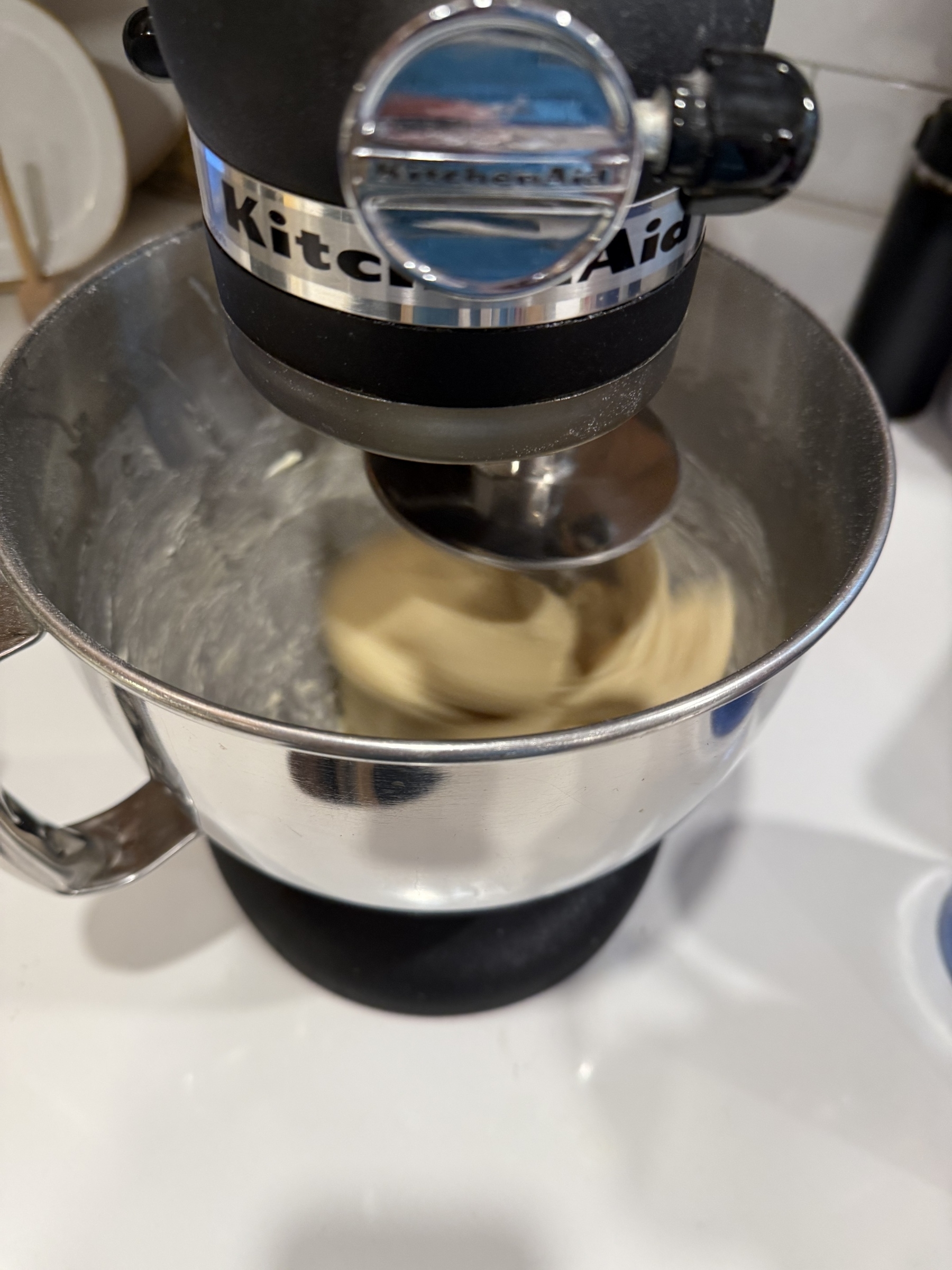 A stand mixer is blending dough in a metal mixing bowl.