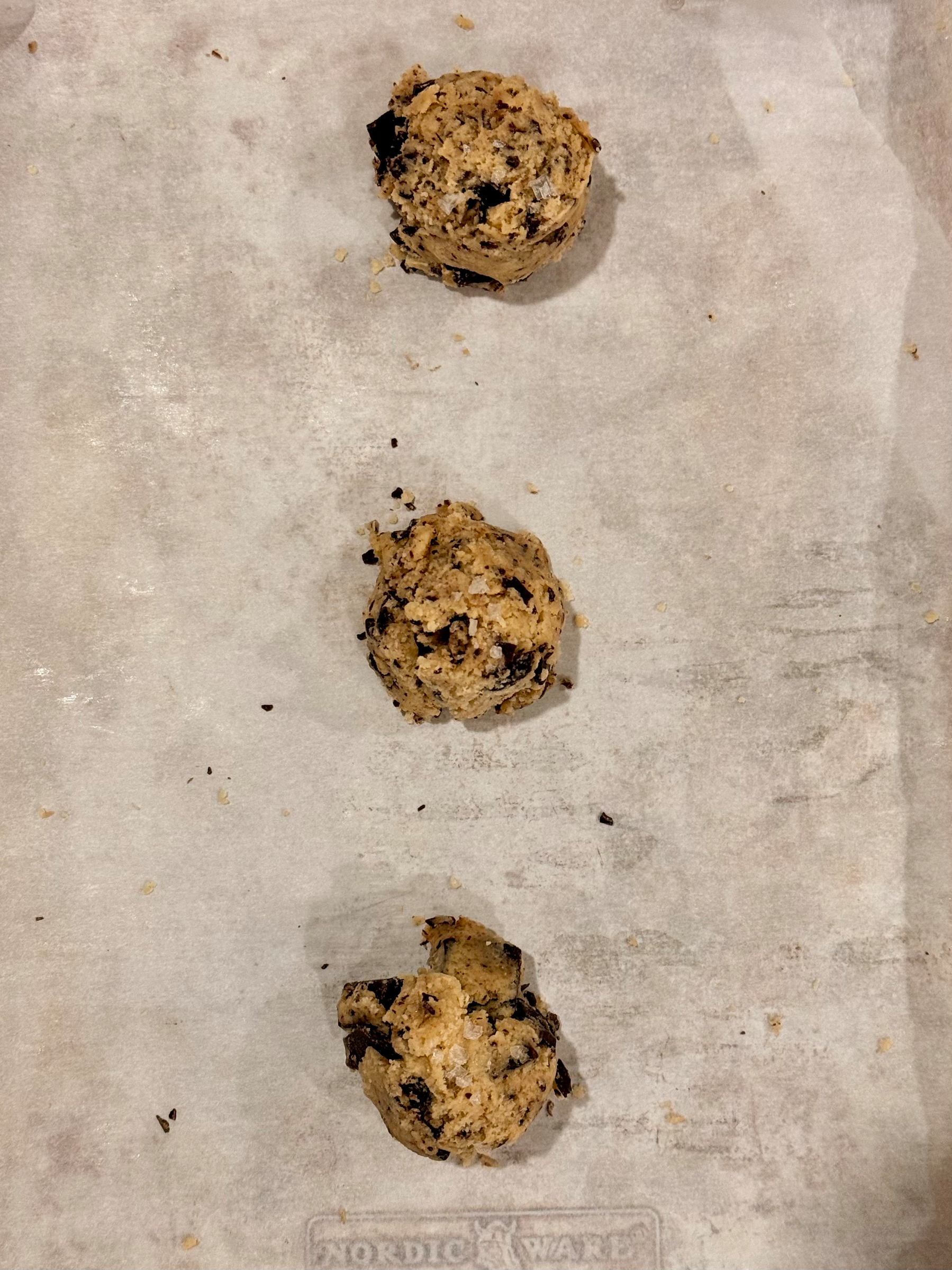 Three scoops of cookie dough are placed on a baking sheet lined with parchment paper.