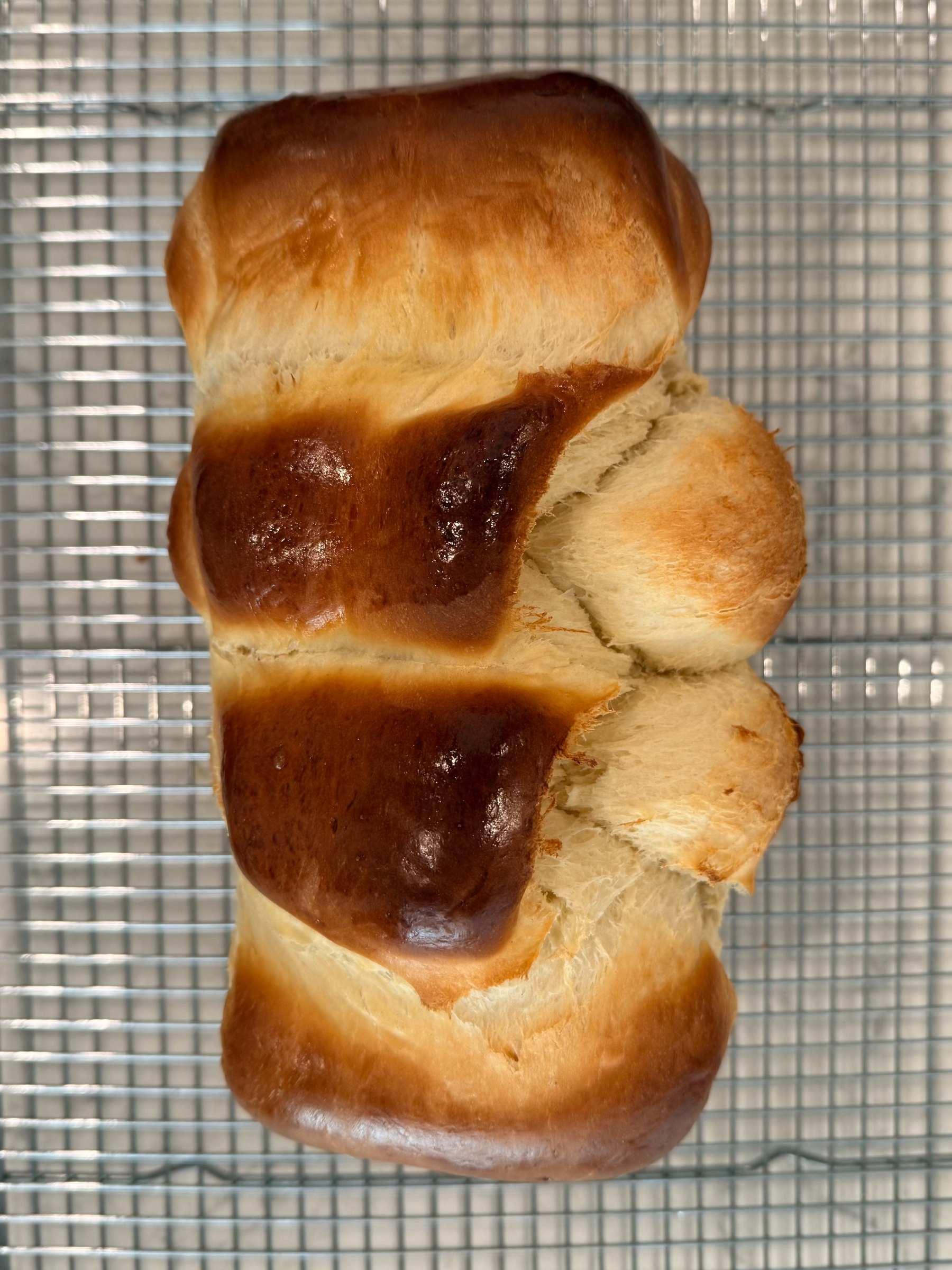 A loaf of golden-brown bread with a glossy top rests on a wire rack. From the top down