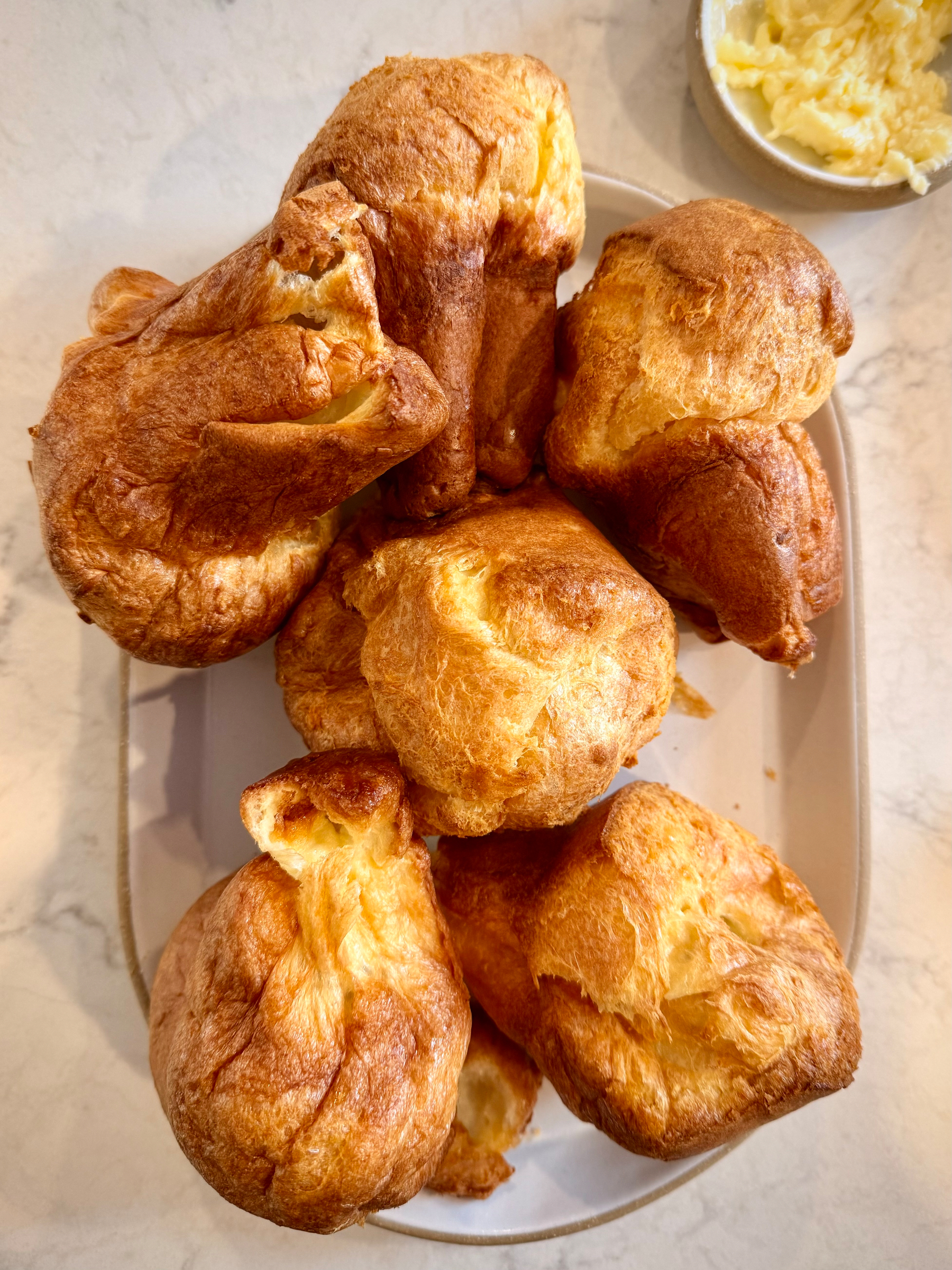 A pile of 6 golden brown popovers photographed from above on a plate 