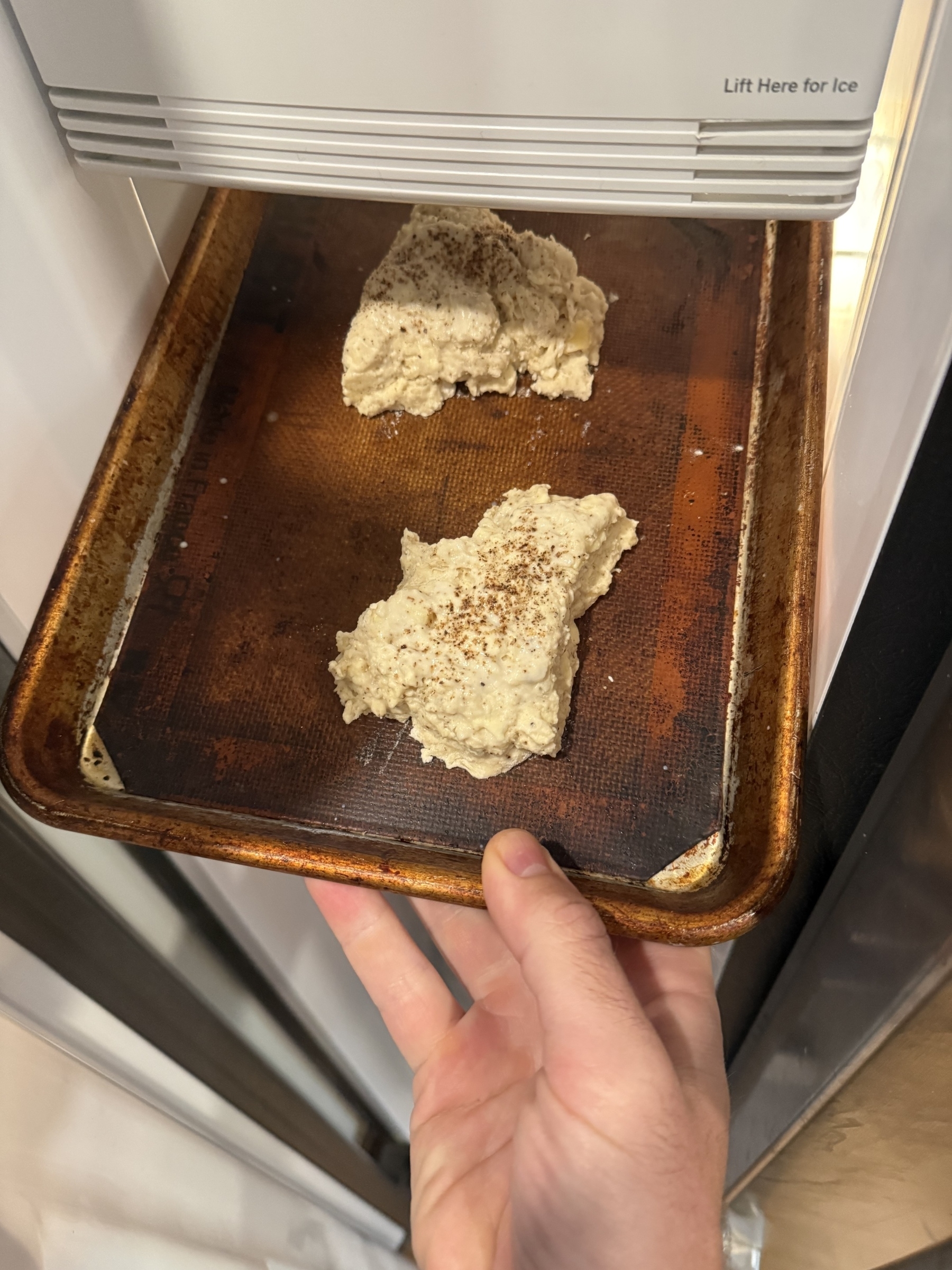 Two pieces of dough with cinnamon on top are placed on a baking sheet inside a freezer.