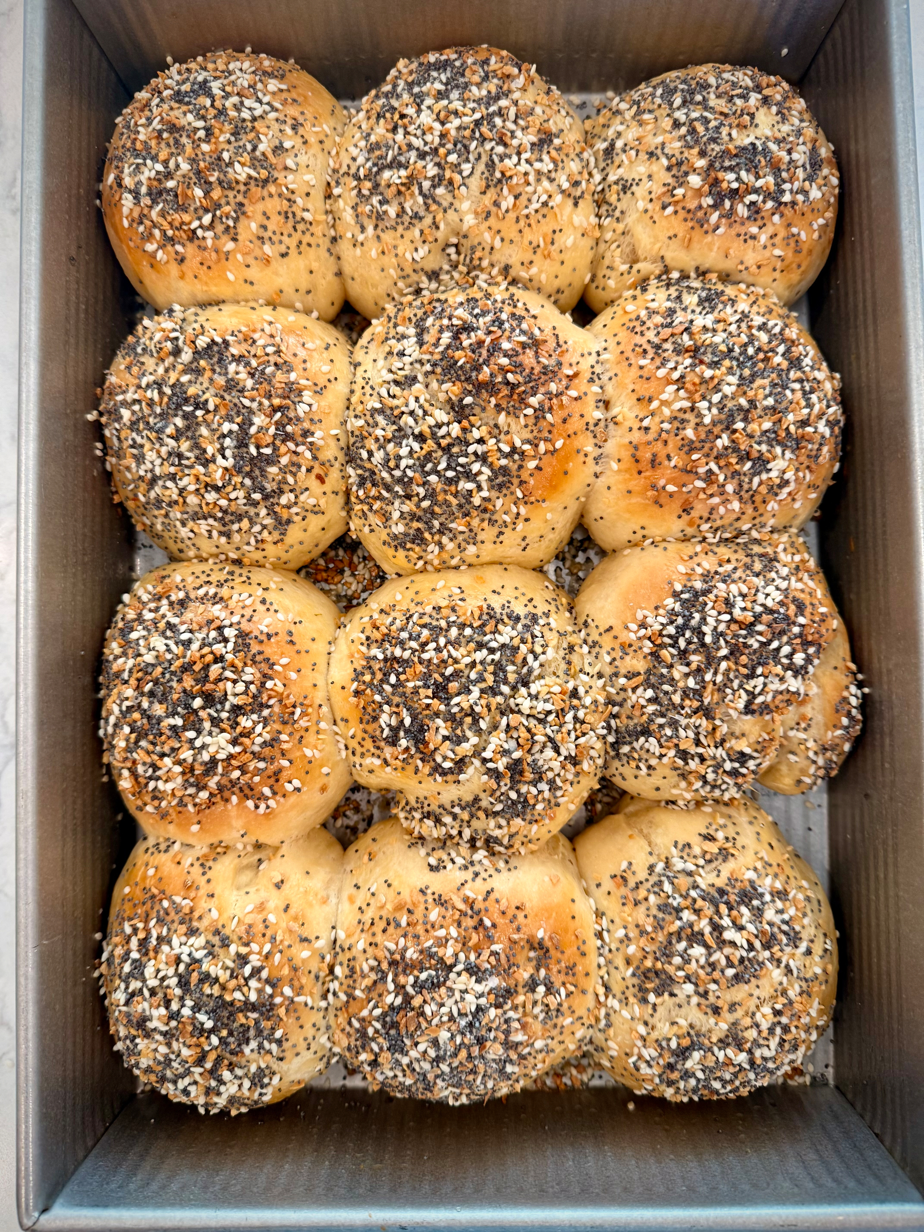 A box contains twelve round, seeded buns arranged neatly in three rows.