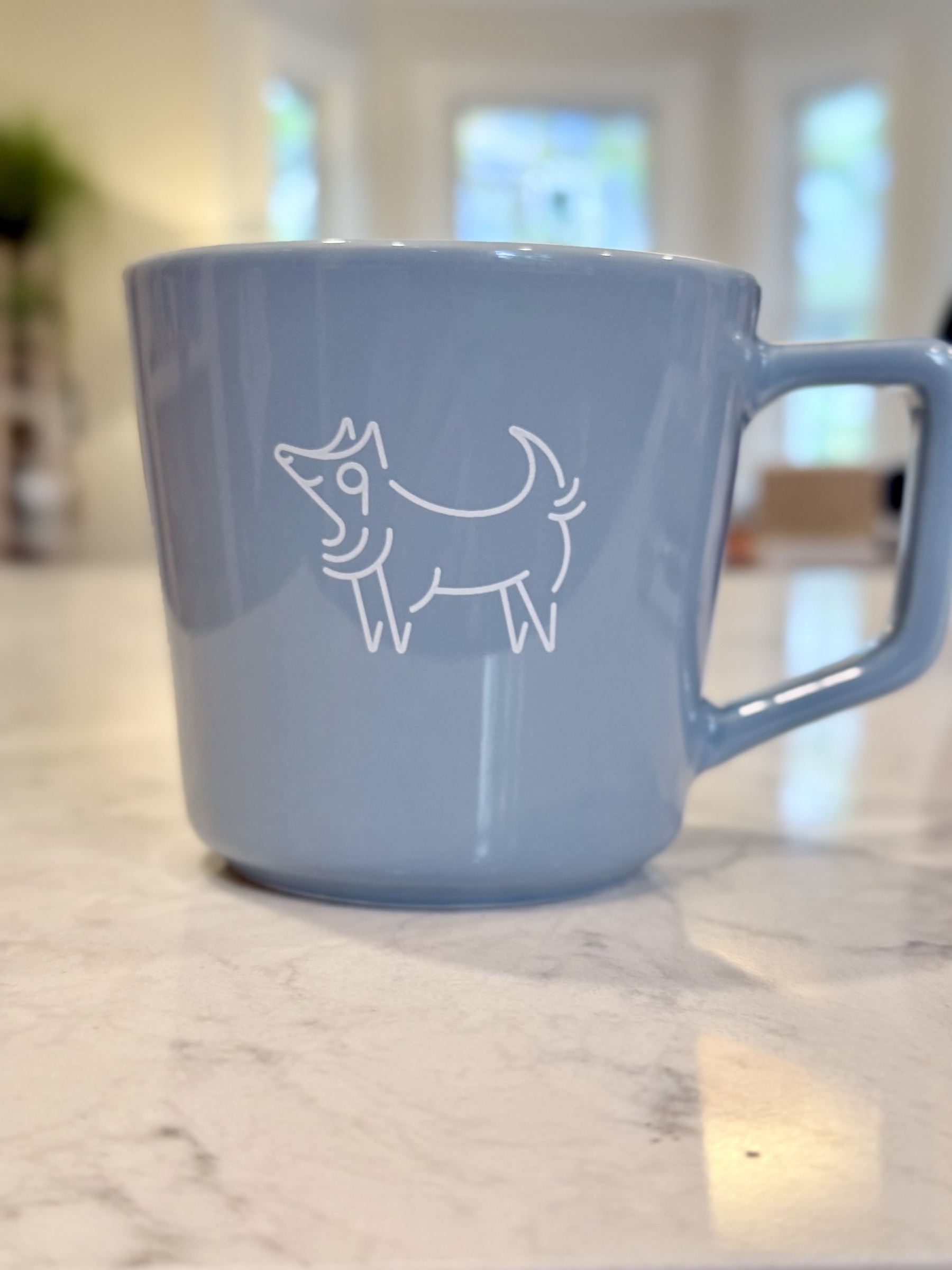 A blue mug with a simple line drawing of a wolf is placed on a marble countertop.