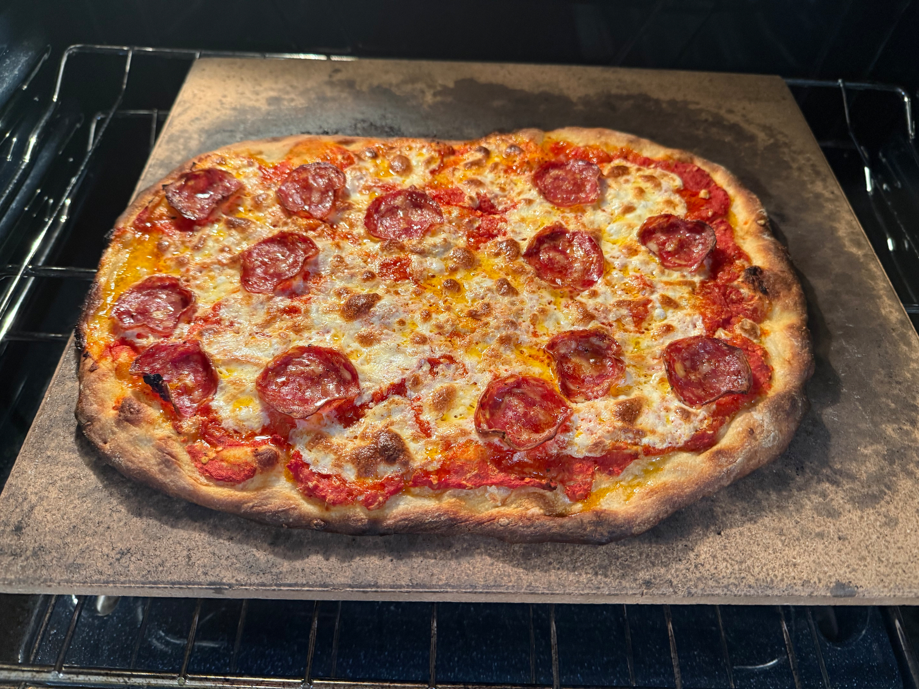 A rectangular pepperoni pizza with melted cheese is baking on a stone in the oven.
