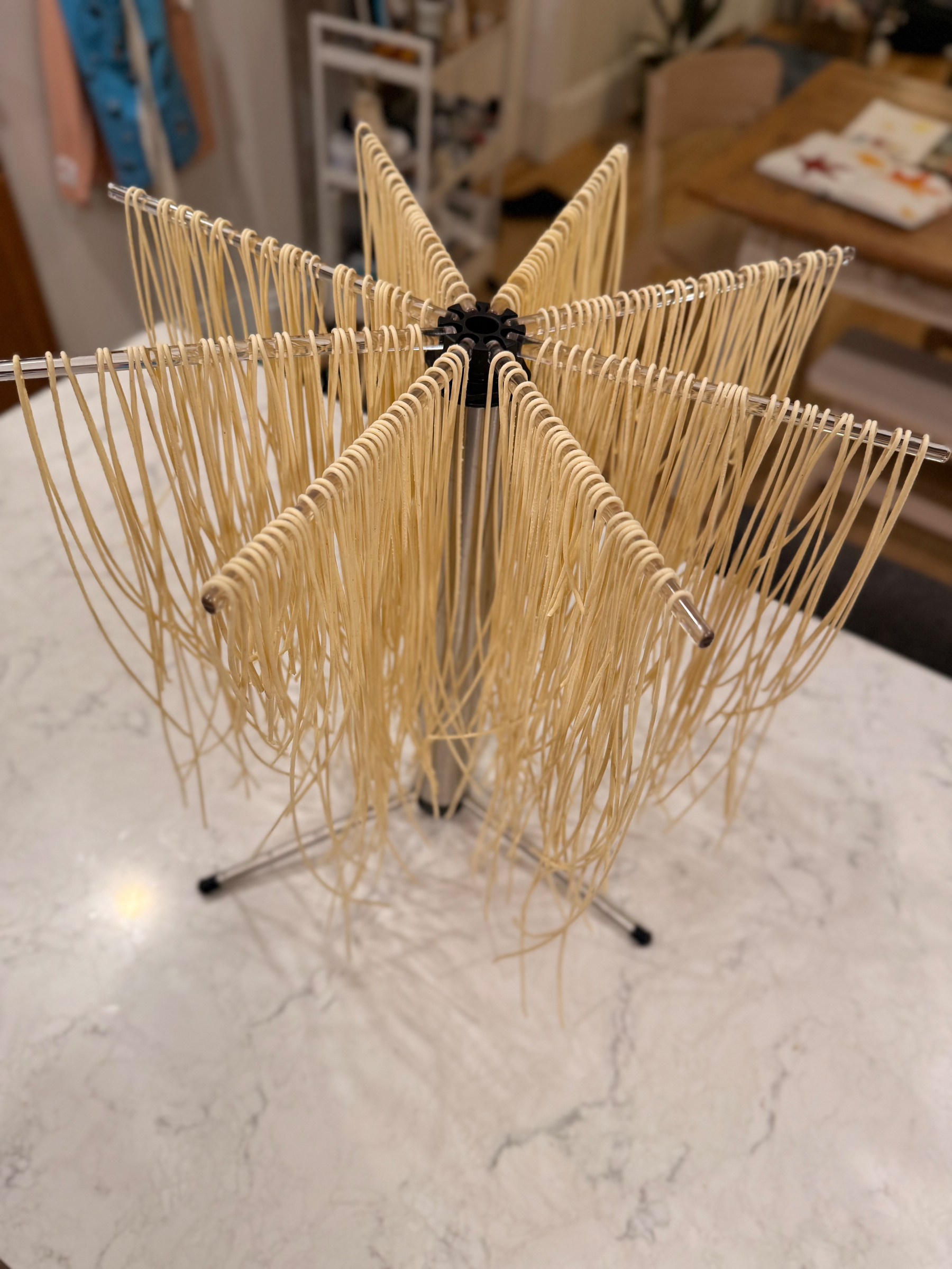 Freshly made pasta is hanging on a drying rack placed on a kitchen counter.