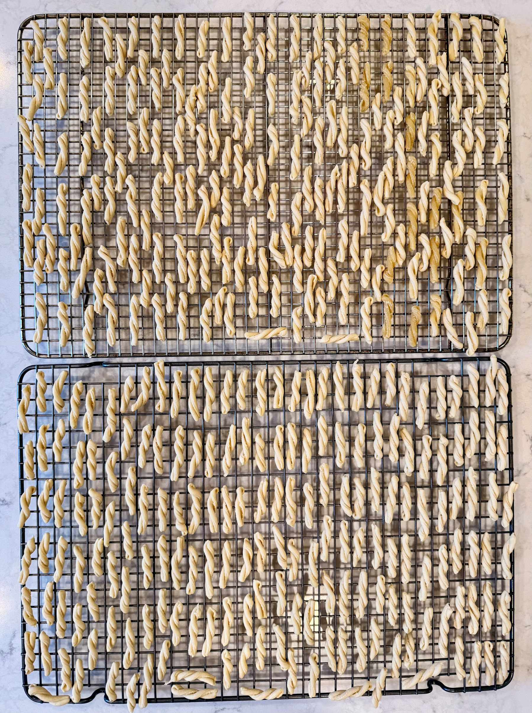 Two cooling racks covered in twisted pasta shapes are set out for drying.