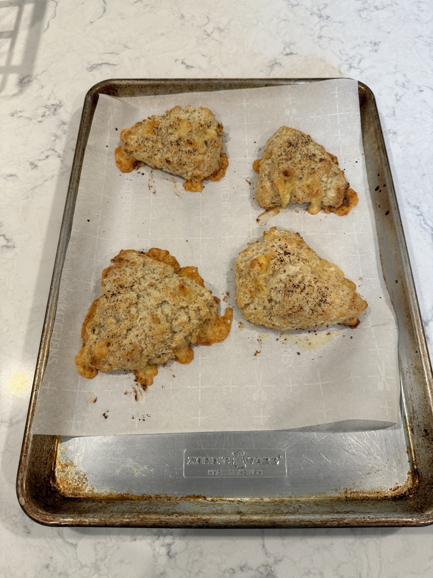 Four baked scones with a rustic appearance are arranged on a parchment-lined baking sheet.
