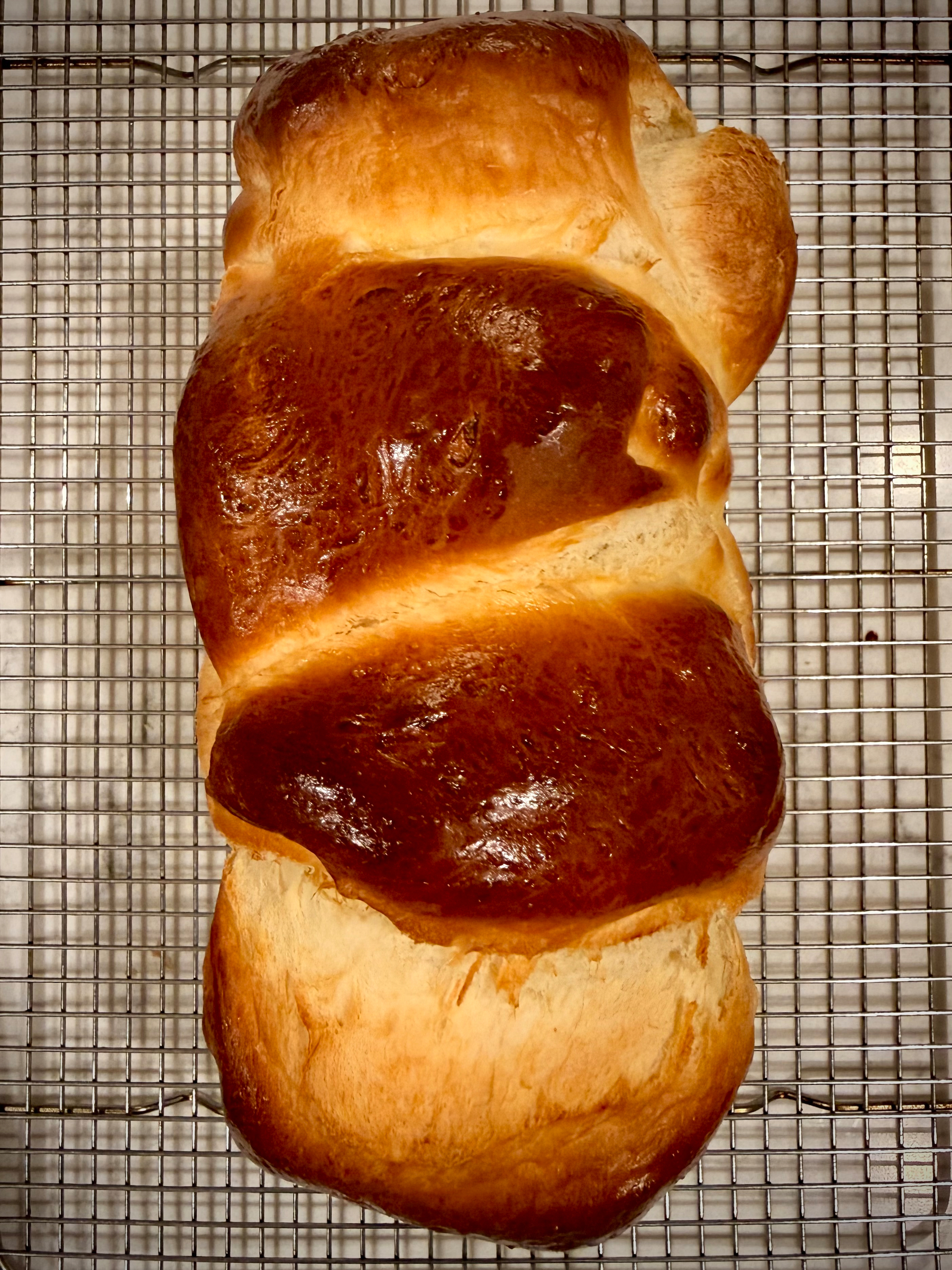A freshly baked loaf of braided bread with a golden brown crust rests on a cooling rack.