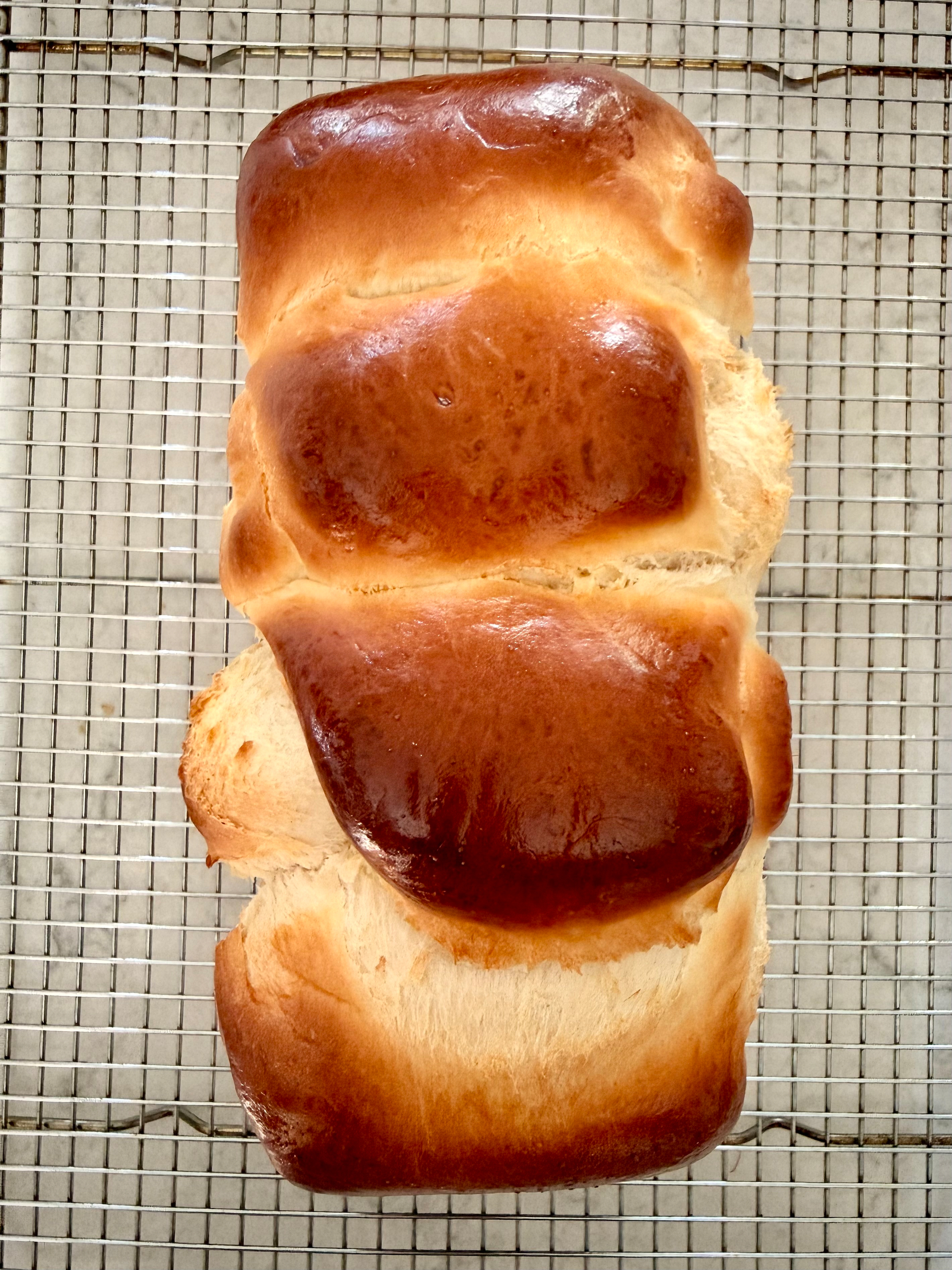 A freshly baked loaf of golden-brown brioche bread rests on a cooling rack.