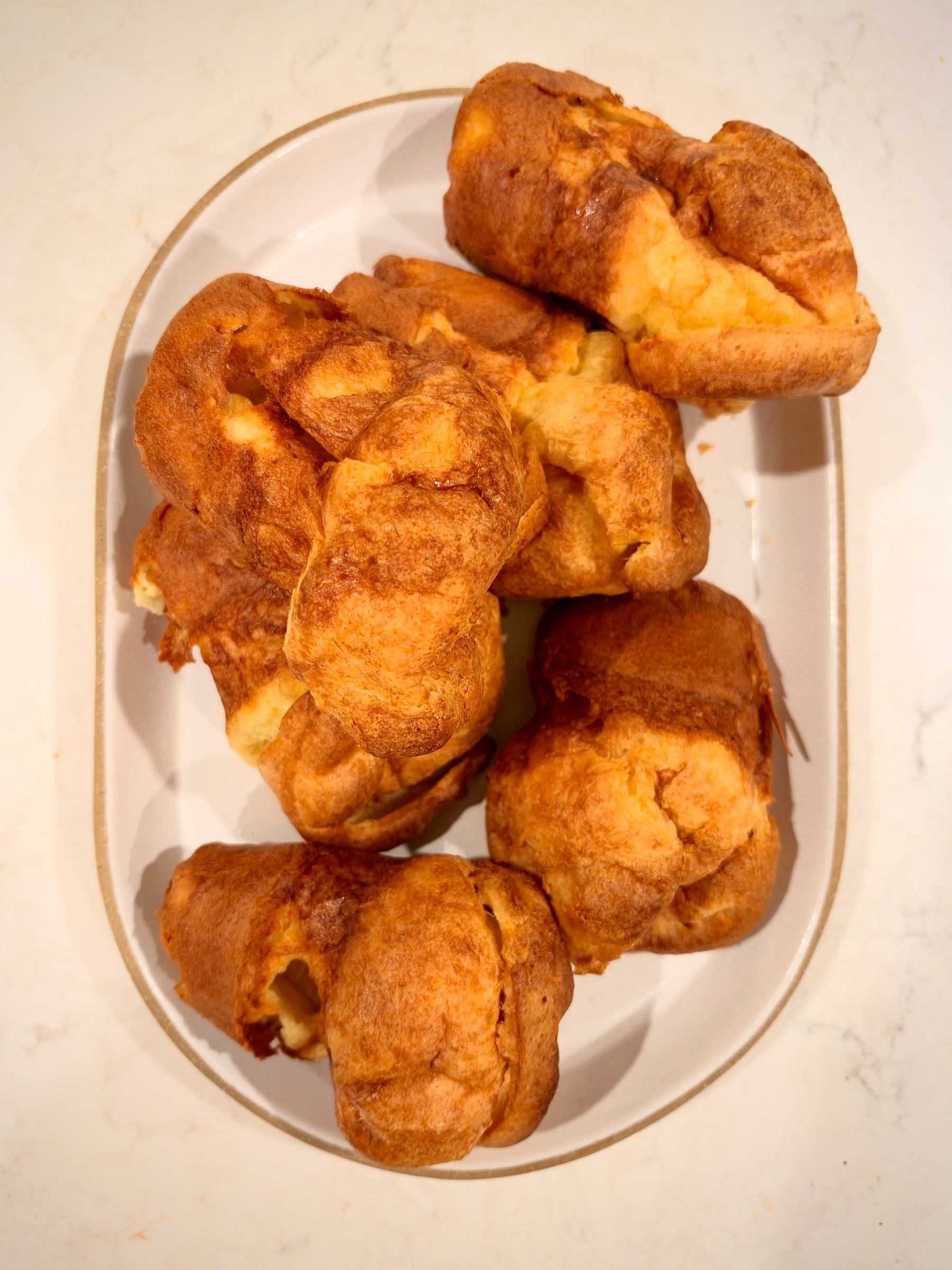 A plate is filled with several golden-brown popovers arranged together.