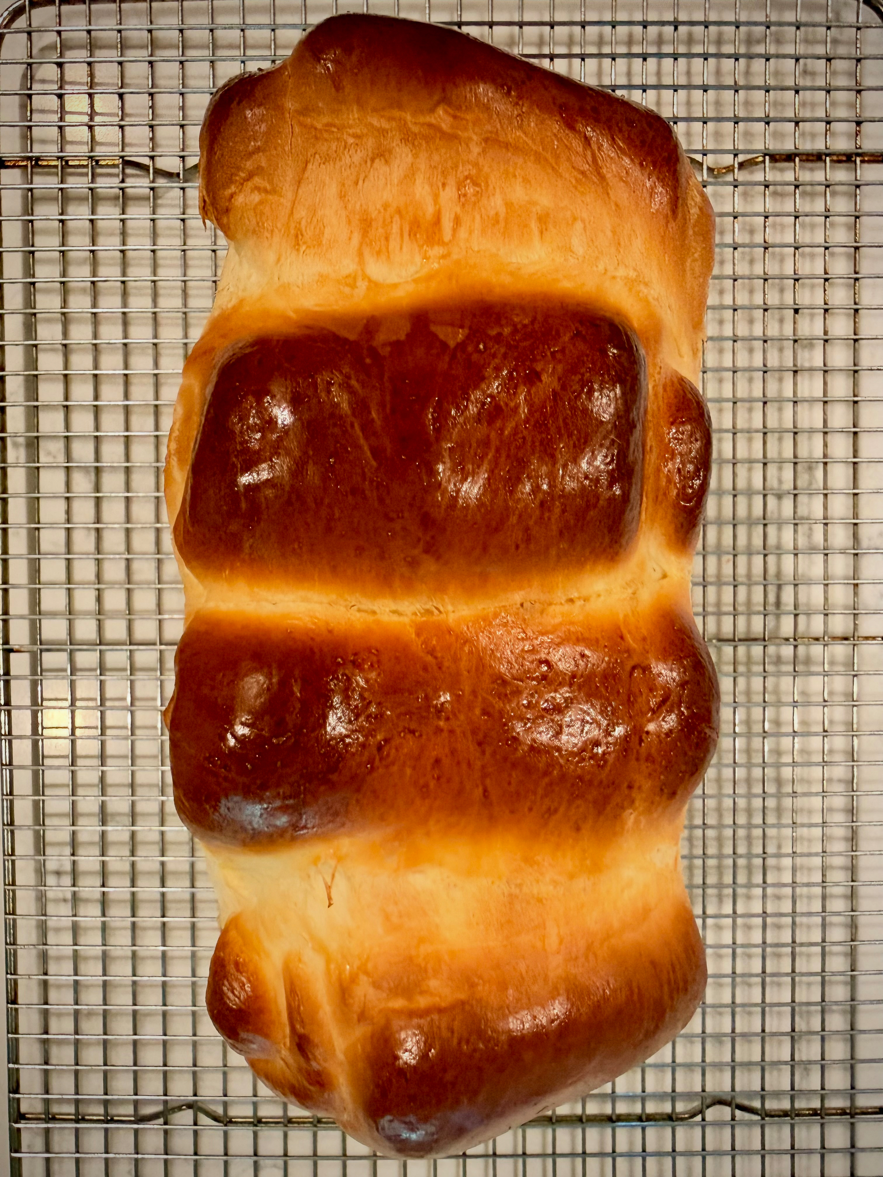 A freshly baked loaf of bread with a golden-brown crust is resting on a cooling rack.